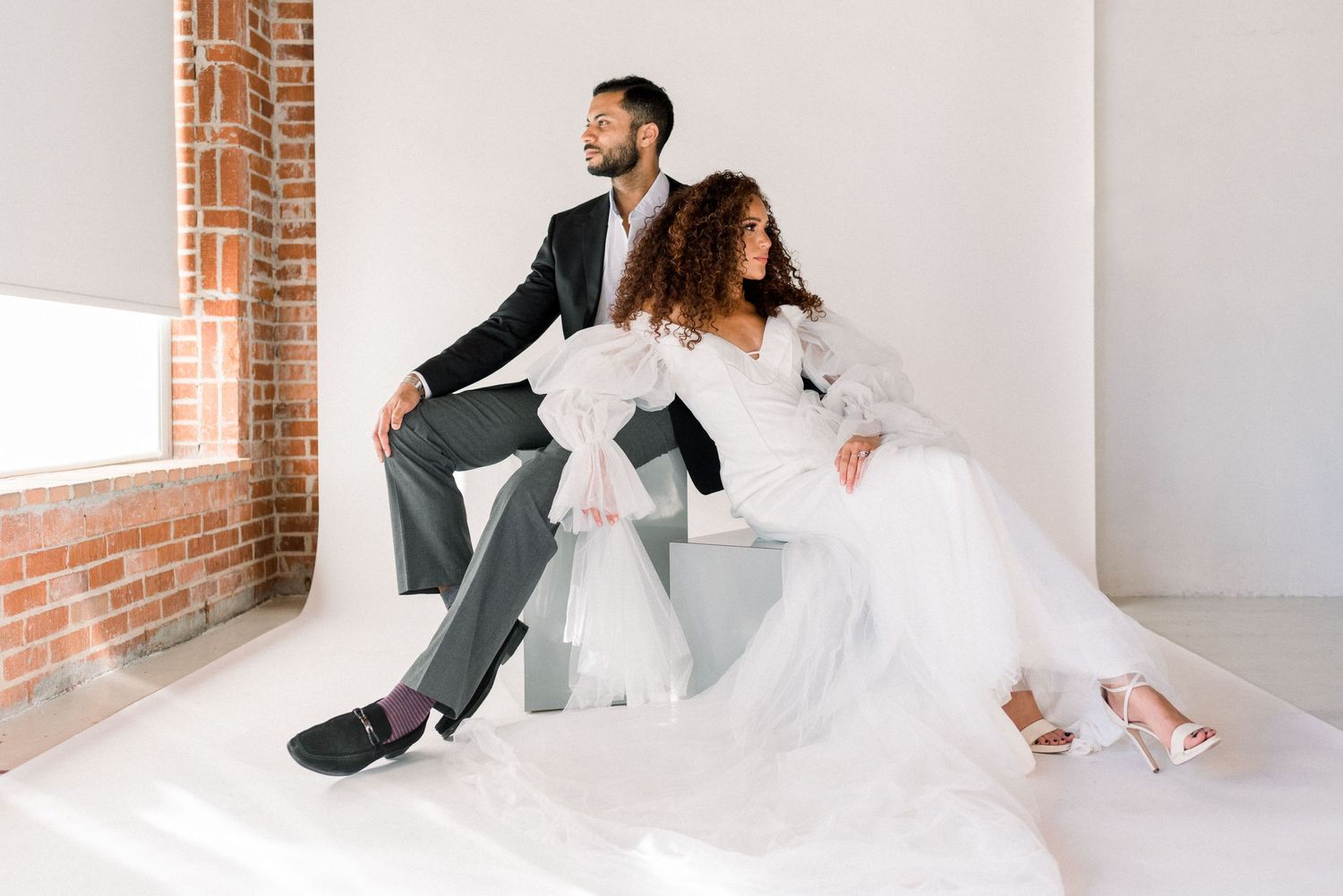 Modern wedding portrait with couple sitting casually against exposed brick wall.