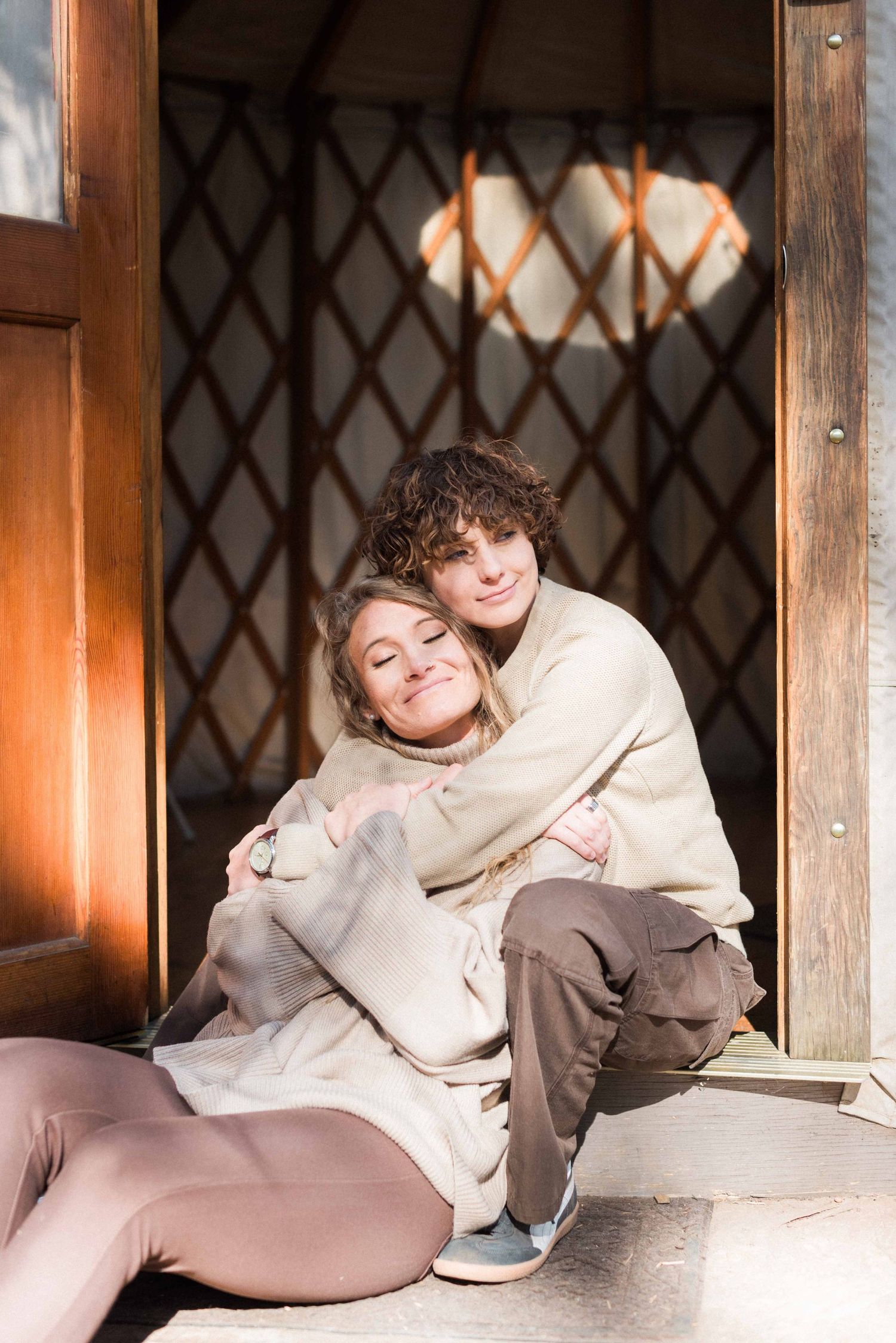 Couple relaxing in rustic yurt doorway wearing matching neutral sweaters.