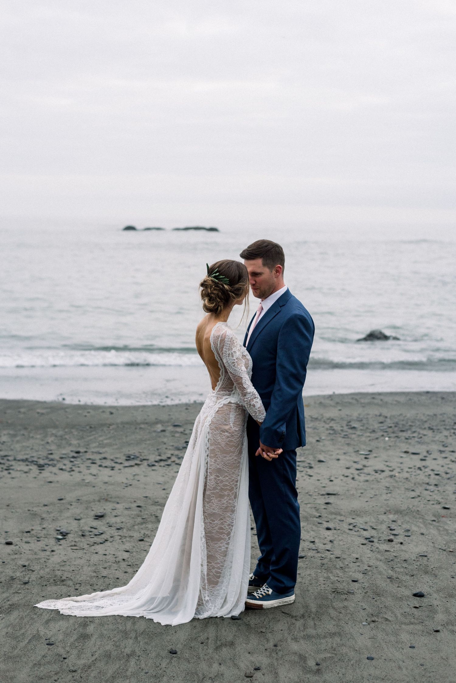 A romantic moment between newlyweds on a misty beach with waves in the background.