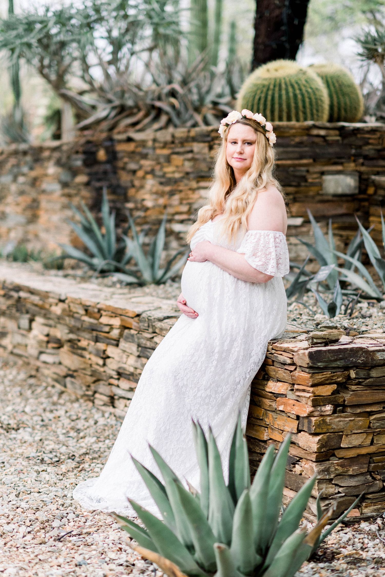 Desert garden maternity photo with stone wall and cacti backdrop.