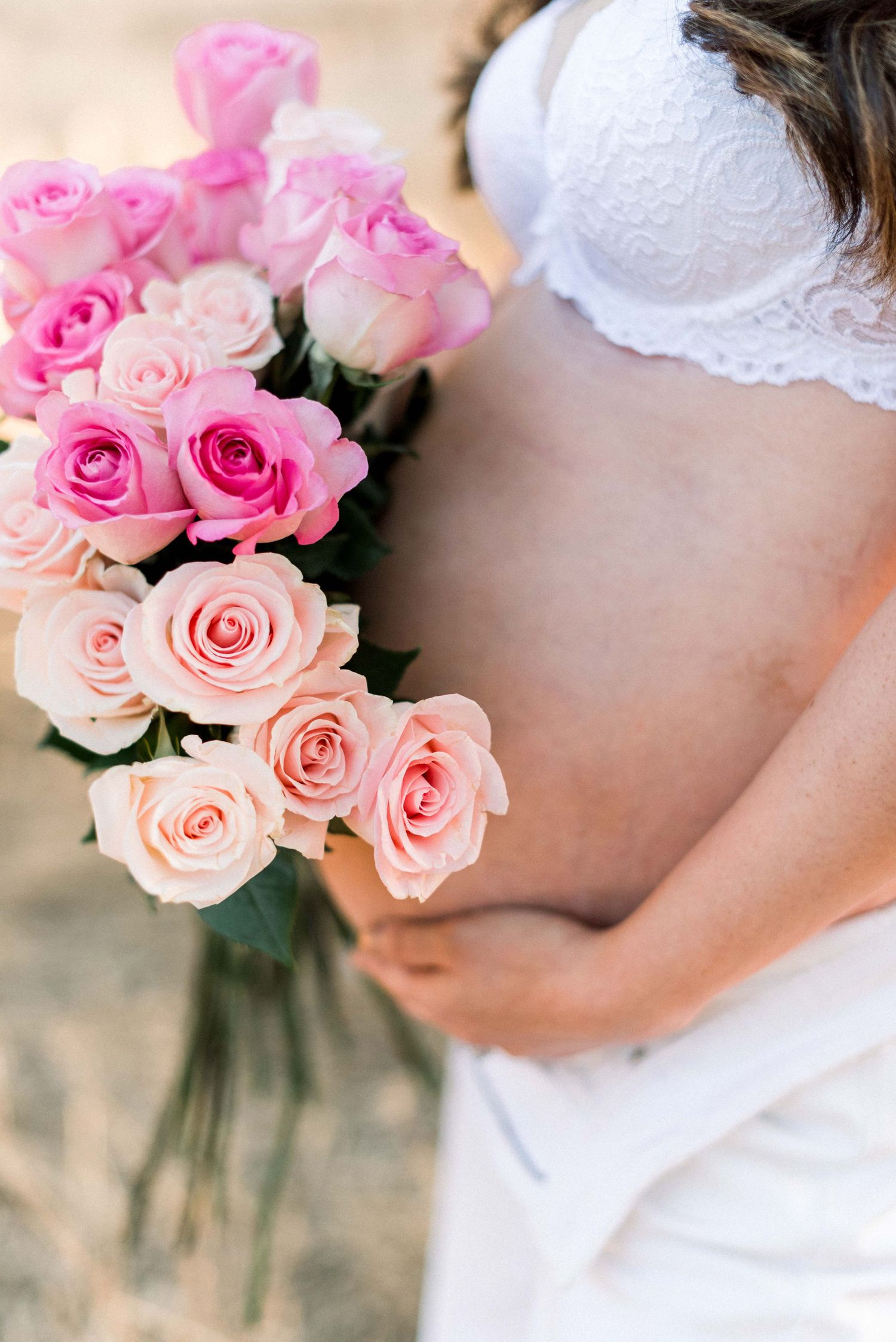 Pink and peach roses bouquet held against white lace garment in soft sunlight.