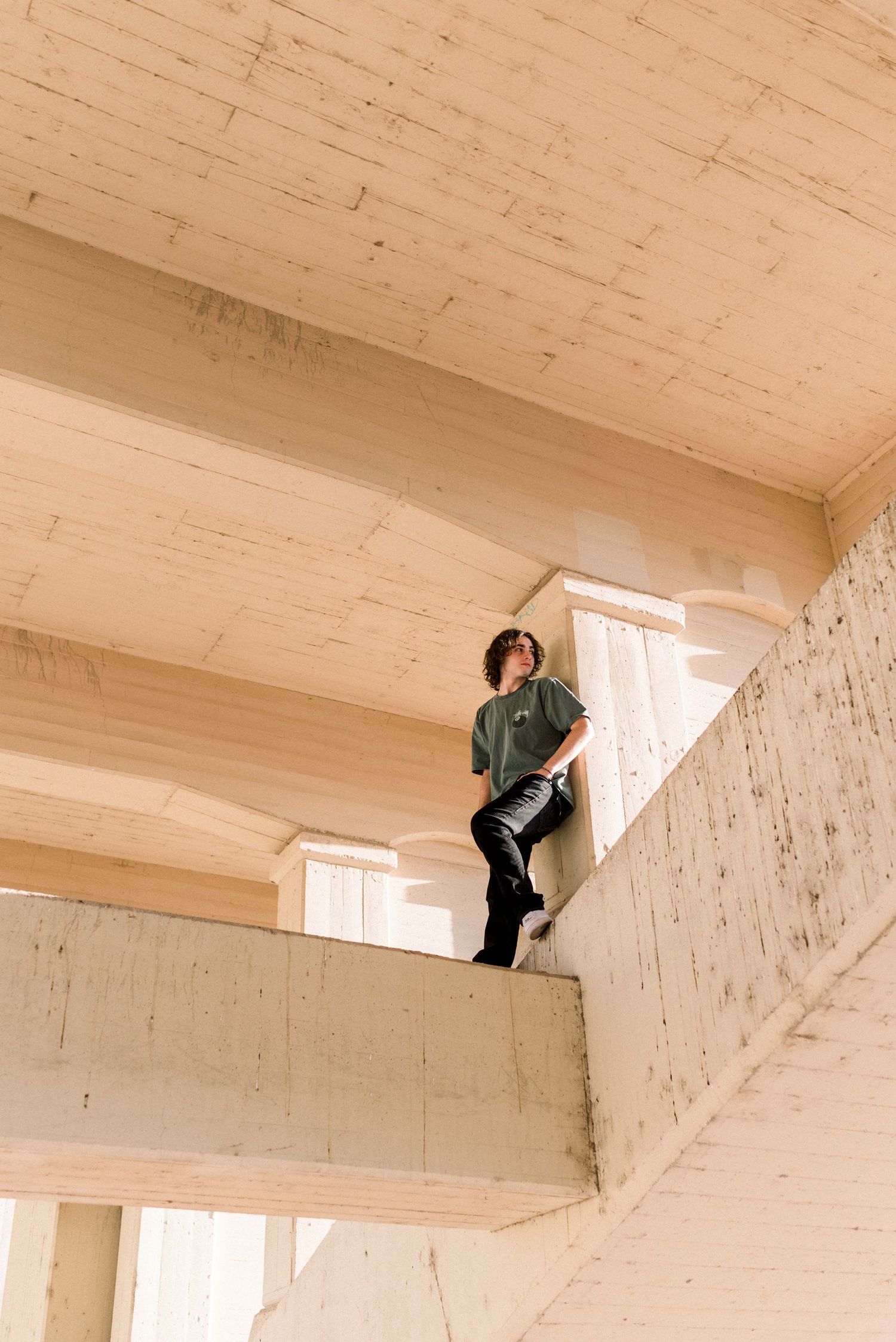 Person in green jacket standing on concrete architectural structure in dramatic lighting.