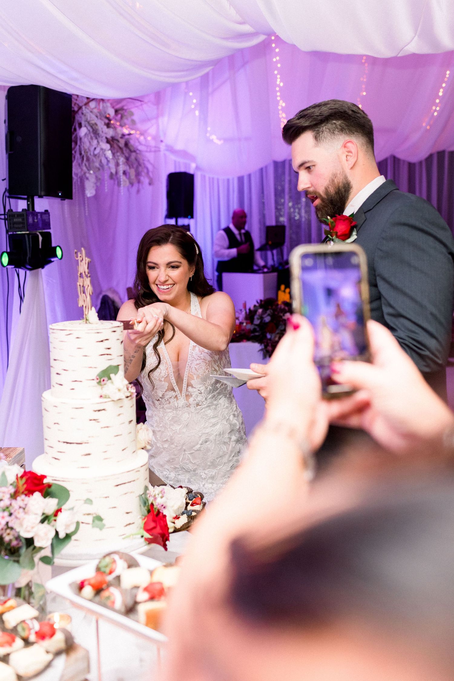 Couple cuts their elegant white birch-textured wedding cake under purple lighting.