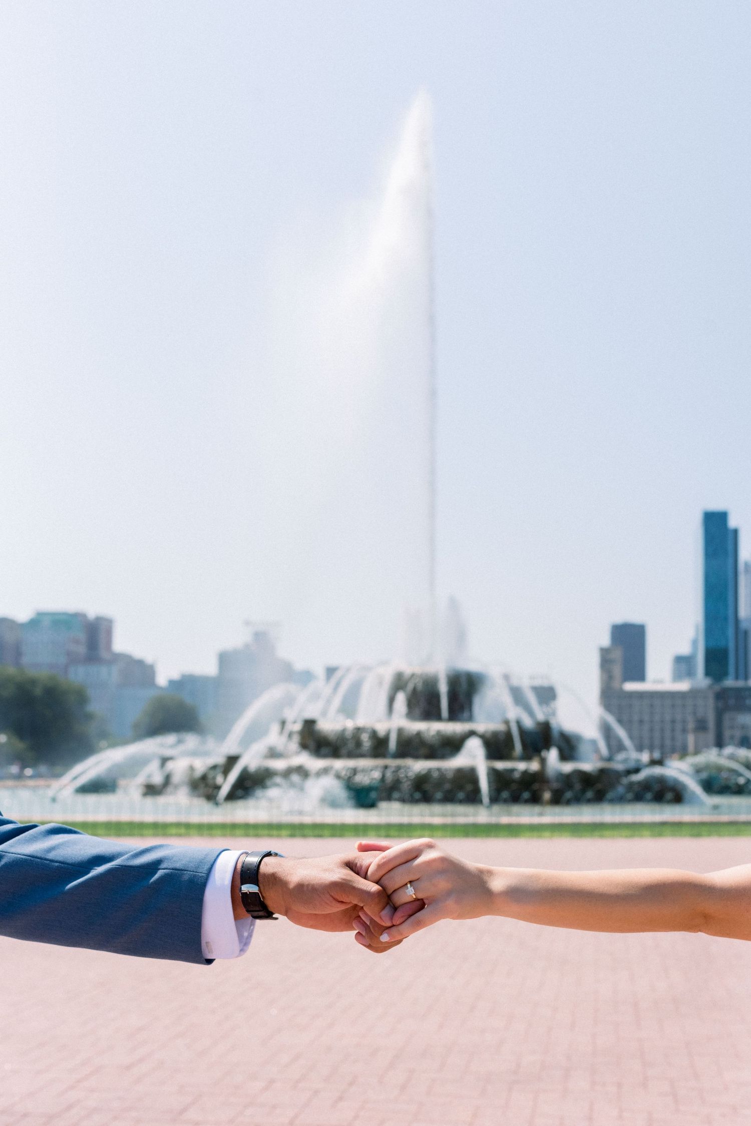 Close-up of couple holding hands with Chicago's Buckingham Fountain and skyline in background.