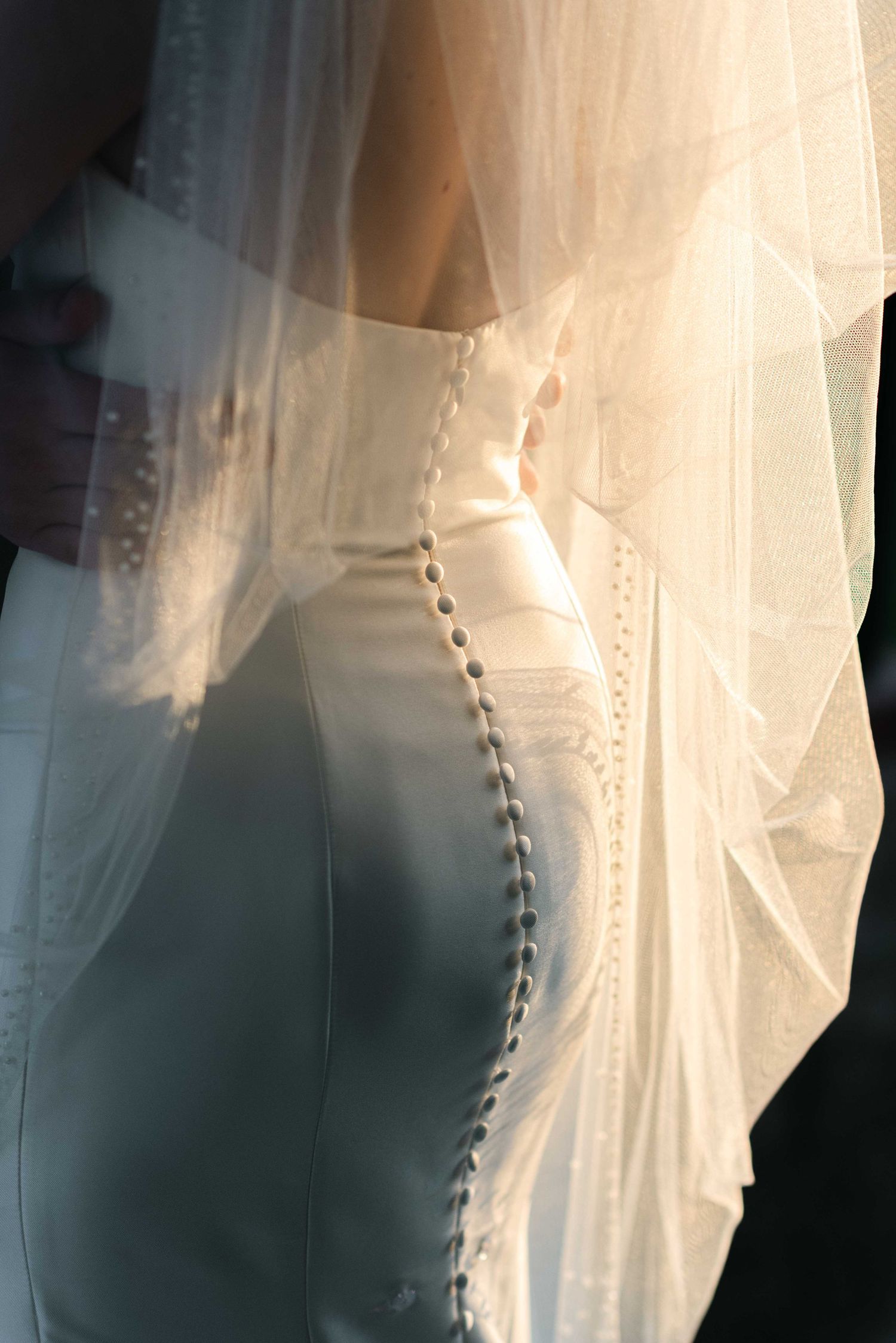 Delicate white lace and buttons detail on a wedding dress veil against a dark background.