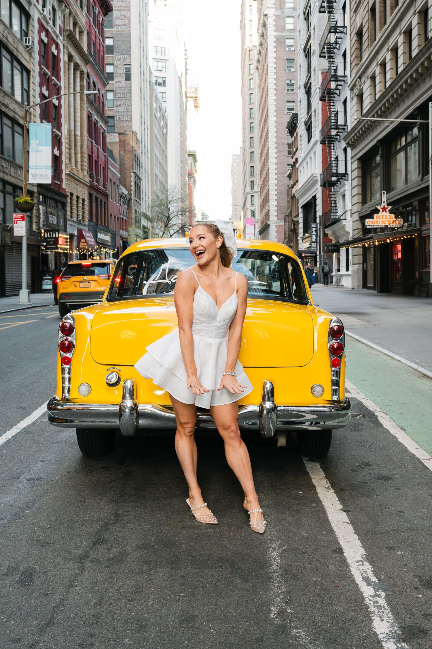 White dress photoshoot with vintage yellow taxi cab on New York City street.
