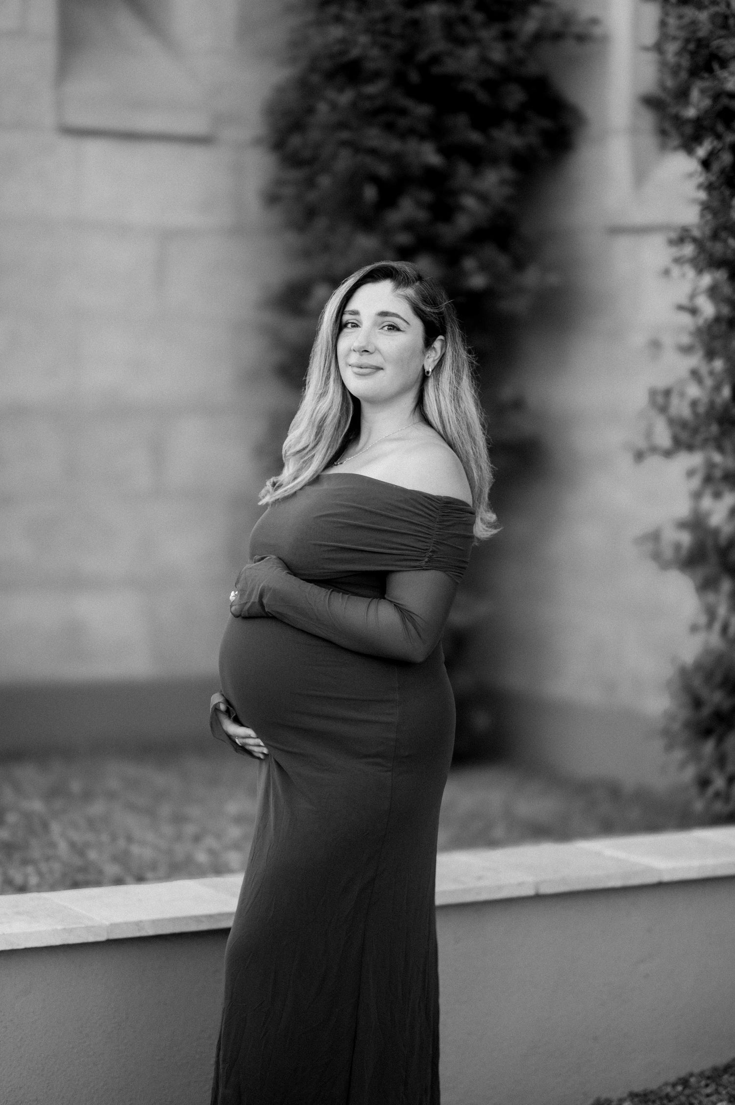 Black and white portrait of someone in a dark dress against a wall.