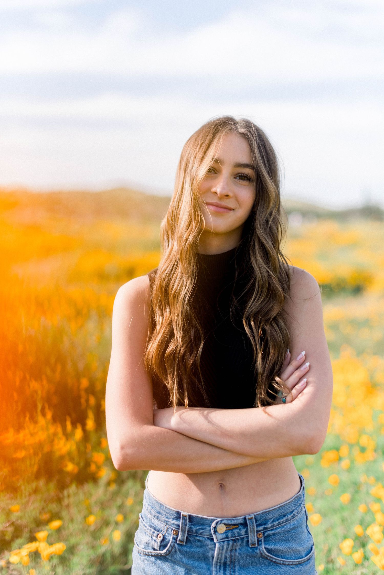 A casual portrait in a black top and jeans amid a field of orange poppies.