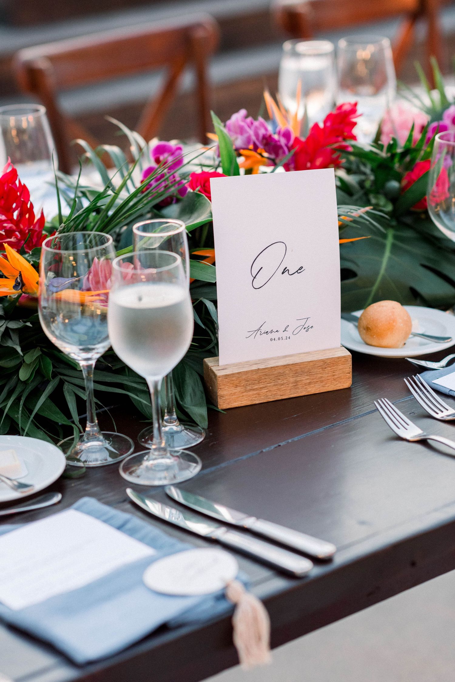 Elegant tropical wedding table setting with bright flowers, wine glasses and place cards in wooden holders.