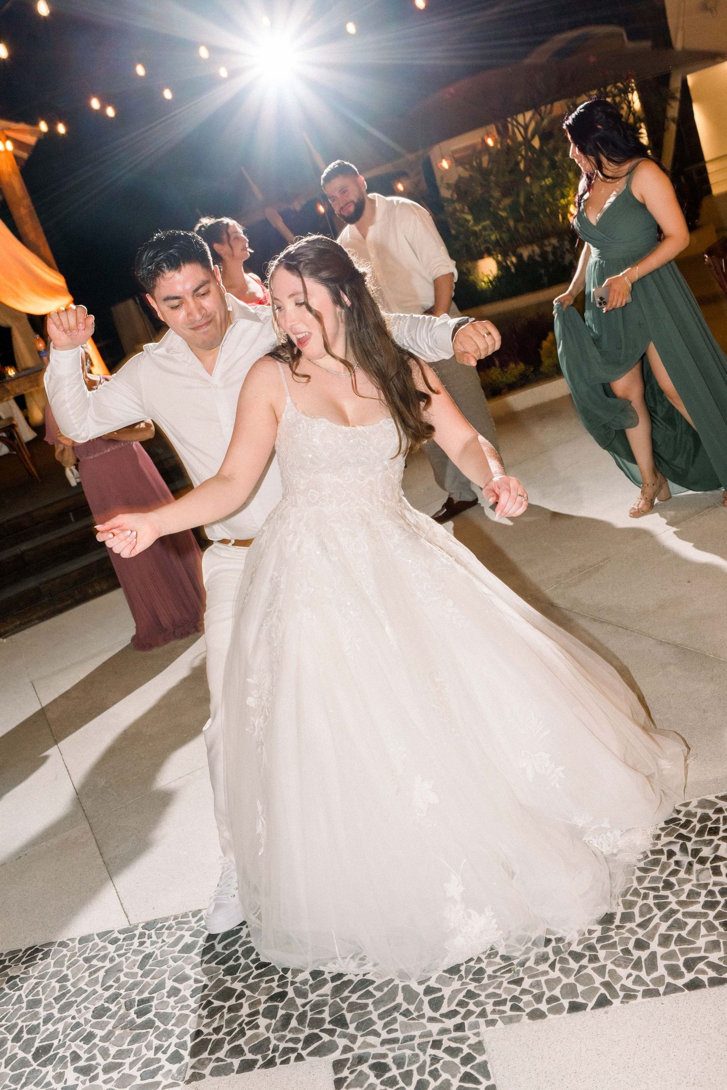 Bride in flowing white gown dances joyfully at outdoor wedding reception.