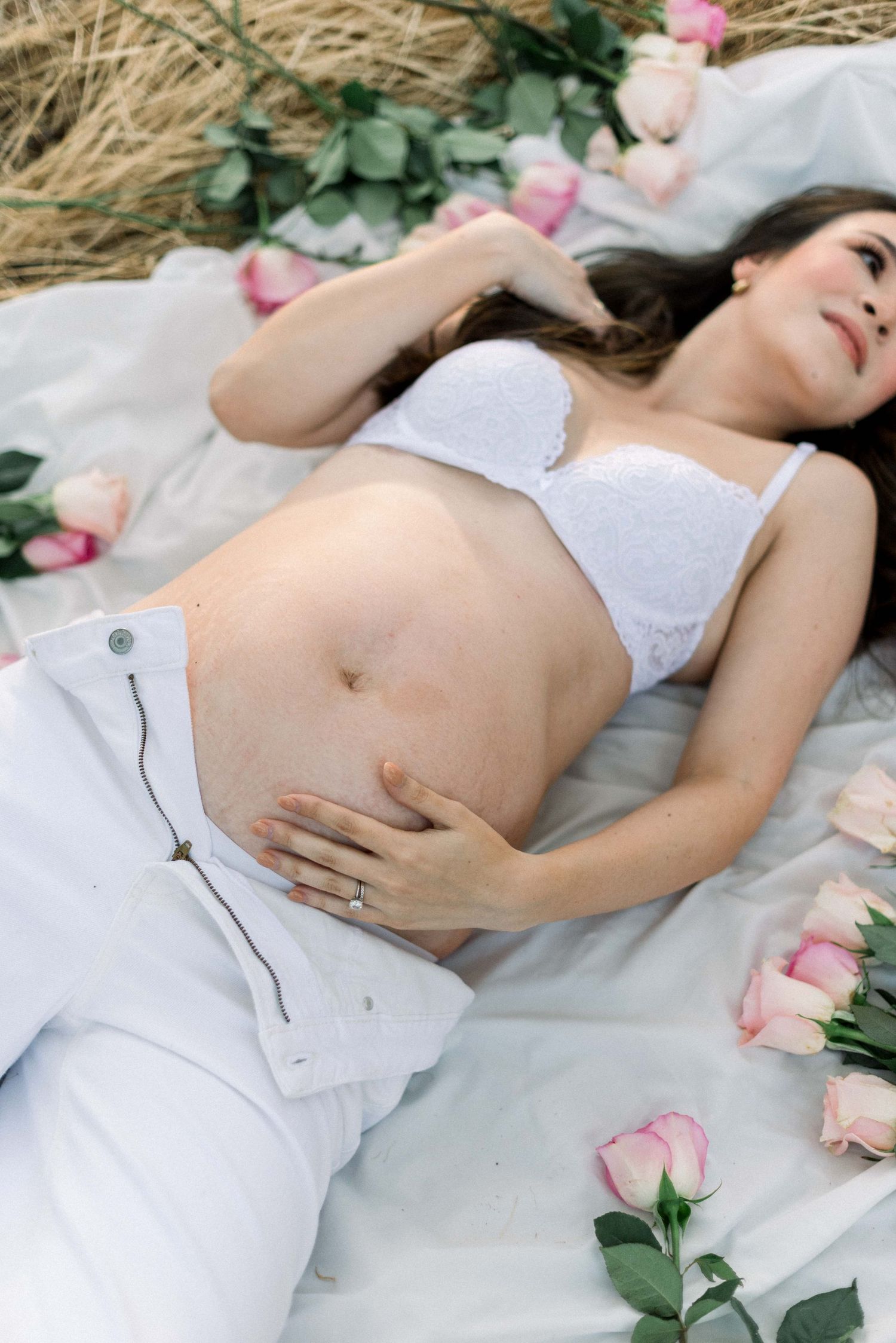 Maternity boudoir photo with pink roses and greenery on white blanket.