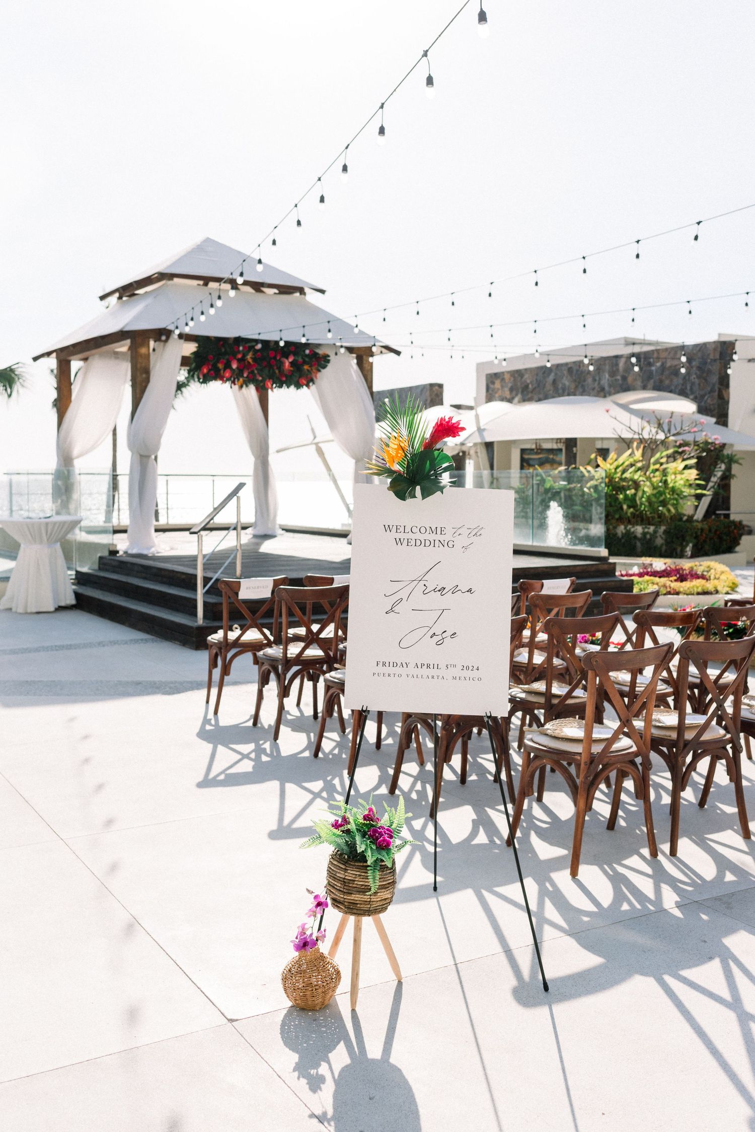 Elegant outdoor wedding ceremony setup with wooden chairs and a white gazebo decorated with flowers and string lights.