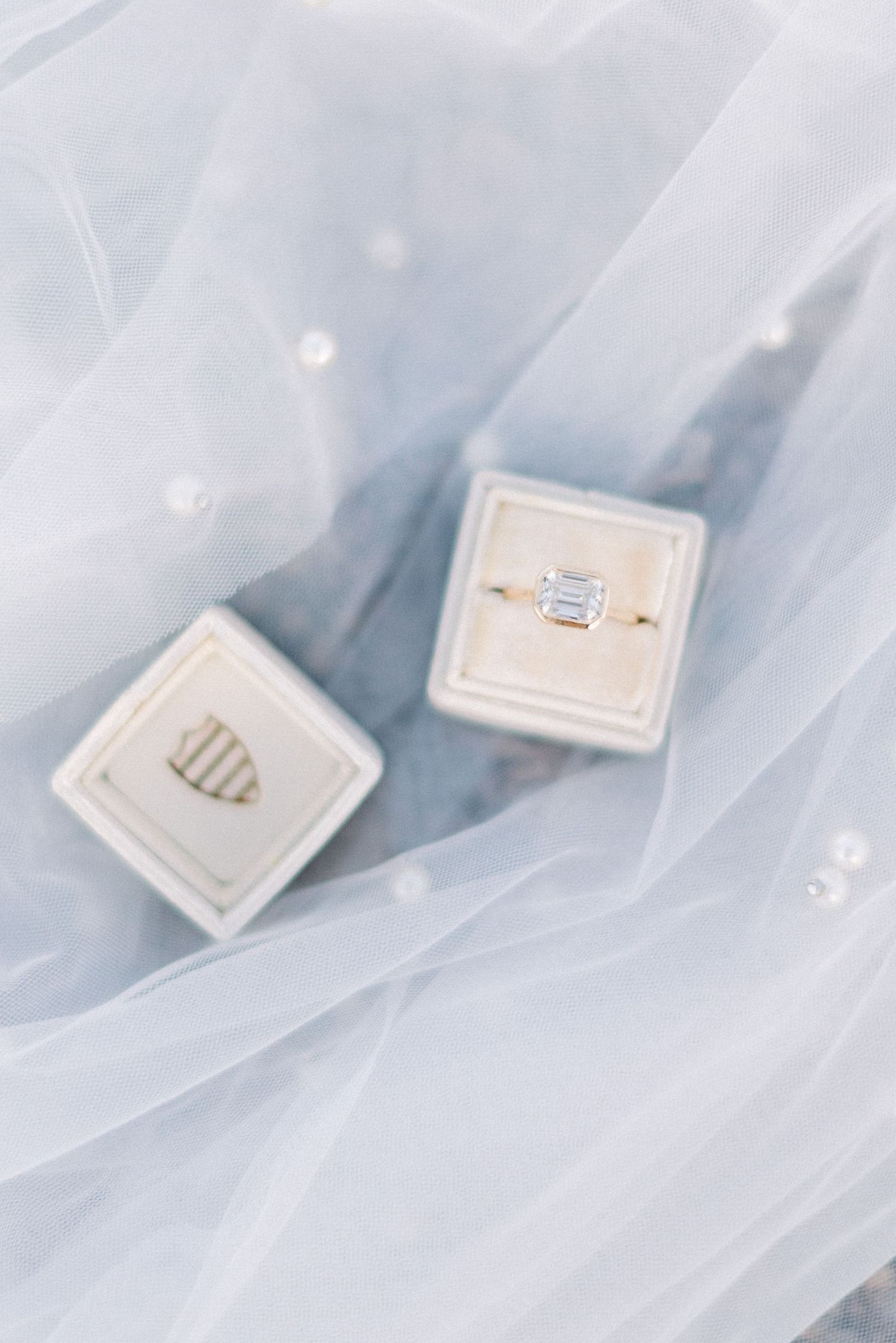 Two elegant ring boxes displayed on ethereal light blue tulle fabric.