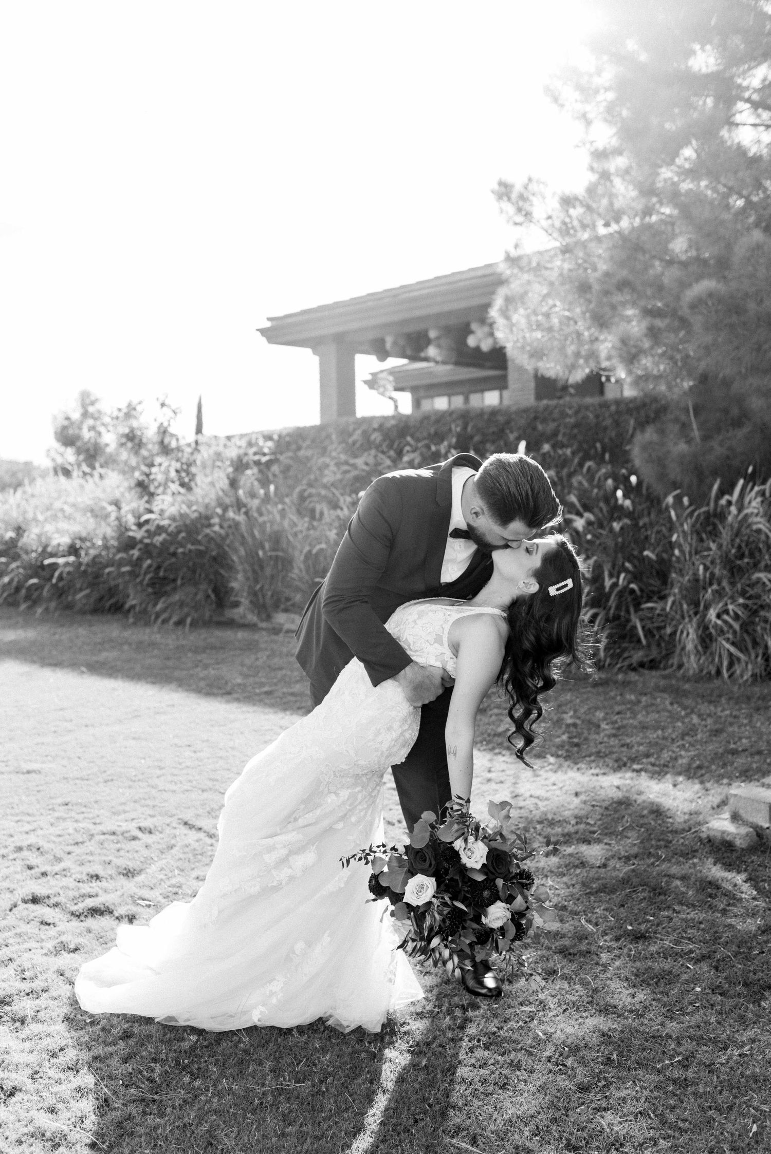 Black and white romantic dip pose with bouquet during outdoor wedding photoshoot.