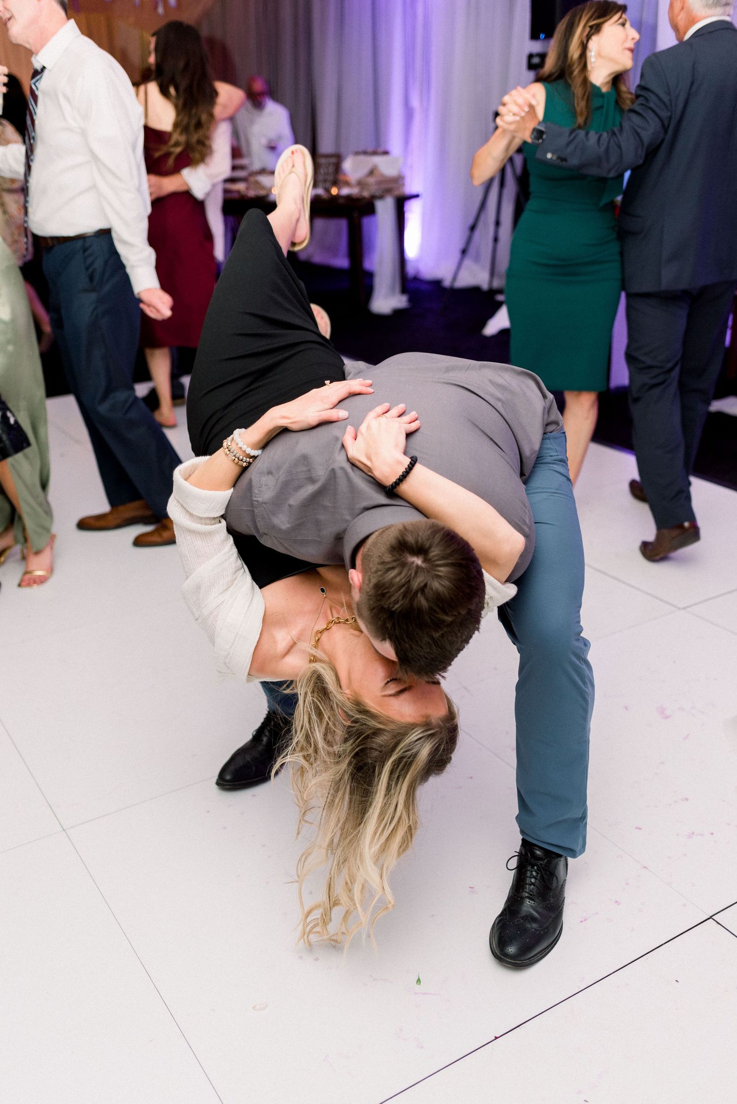 Couple performs dramatic dip dance move on wedding reception dance floor.