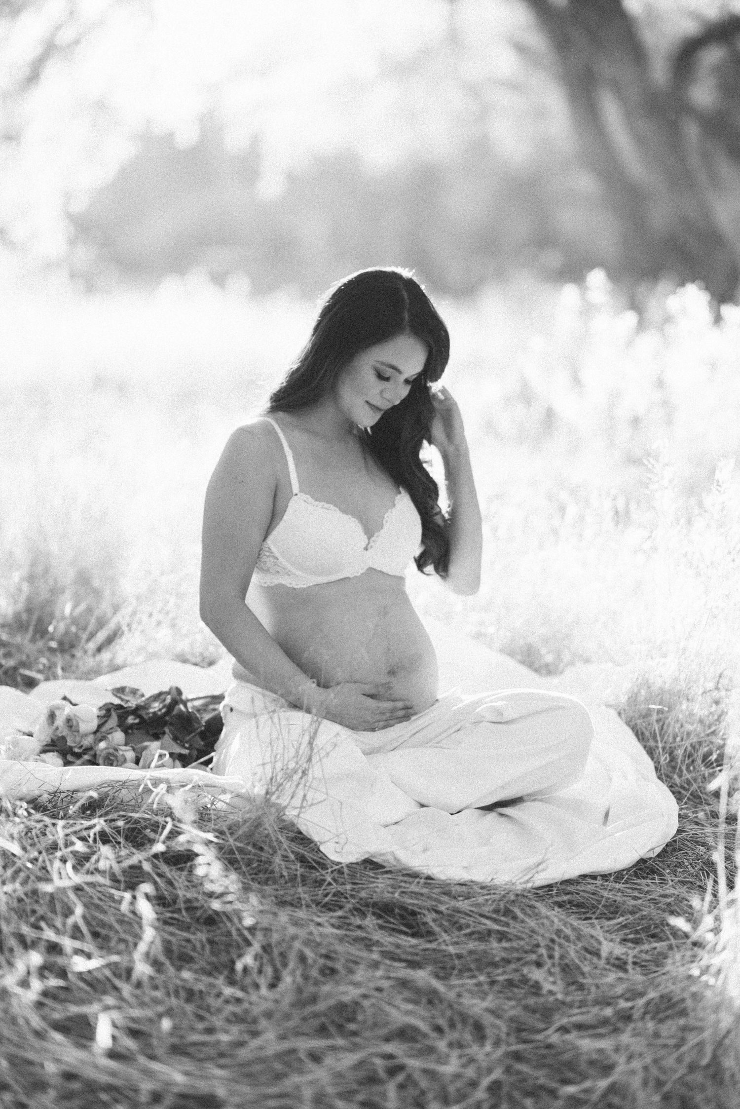 Black and white artistic portrait series of a woman in a white dress reclining in a sunlit meadow.