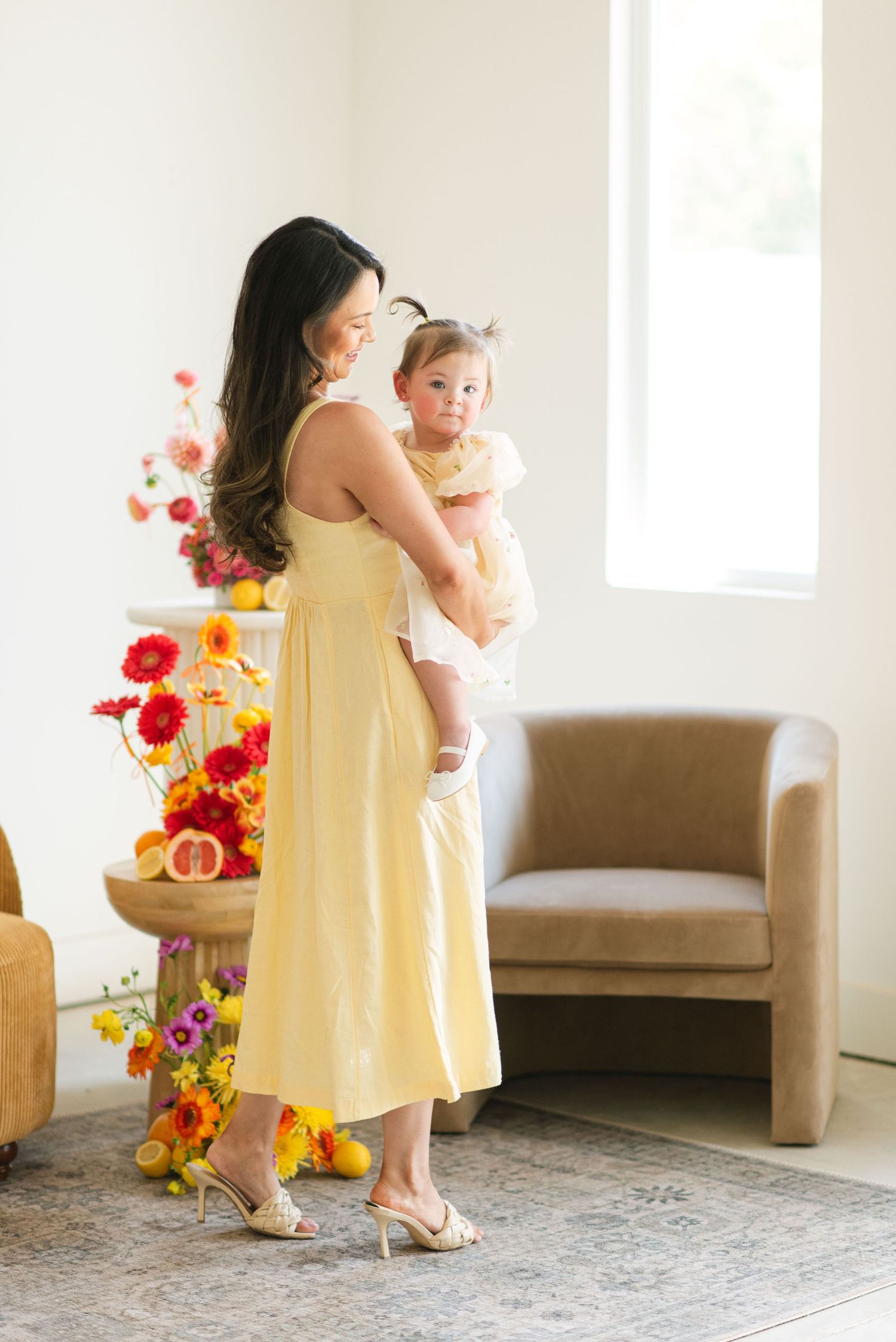 Parent and child in matching yellow dresses dance together in a bright room with colorful floral arrangements.