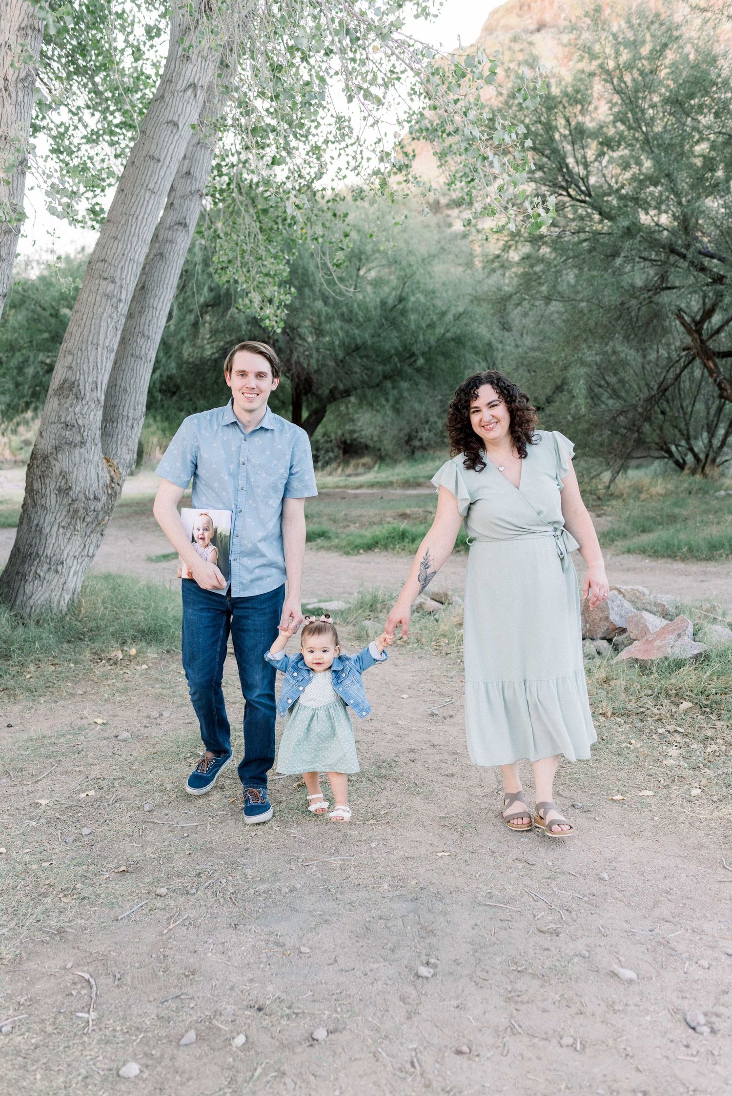 Family in coordinating blue and gray outfits walks together on a dirt path surrounded by trees in a natural setting.