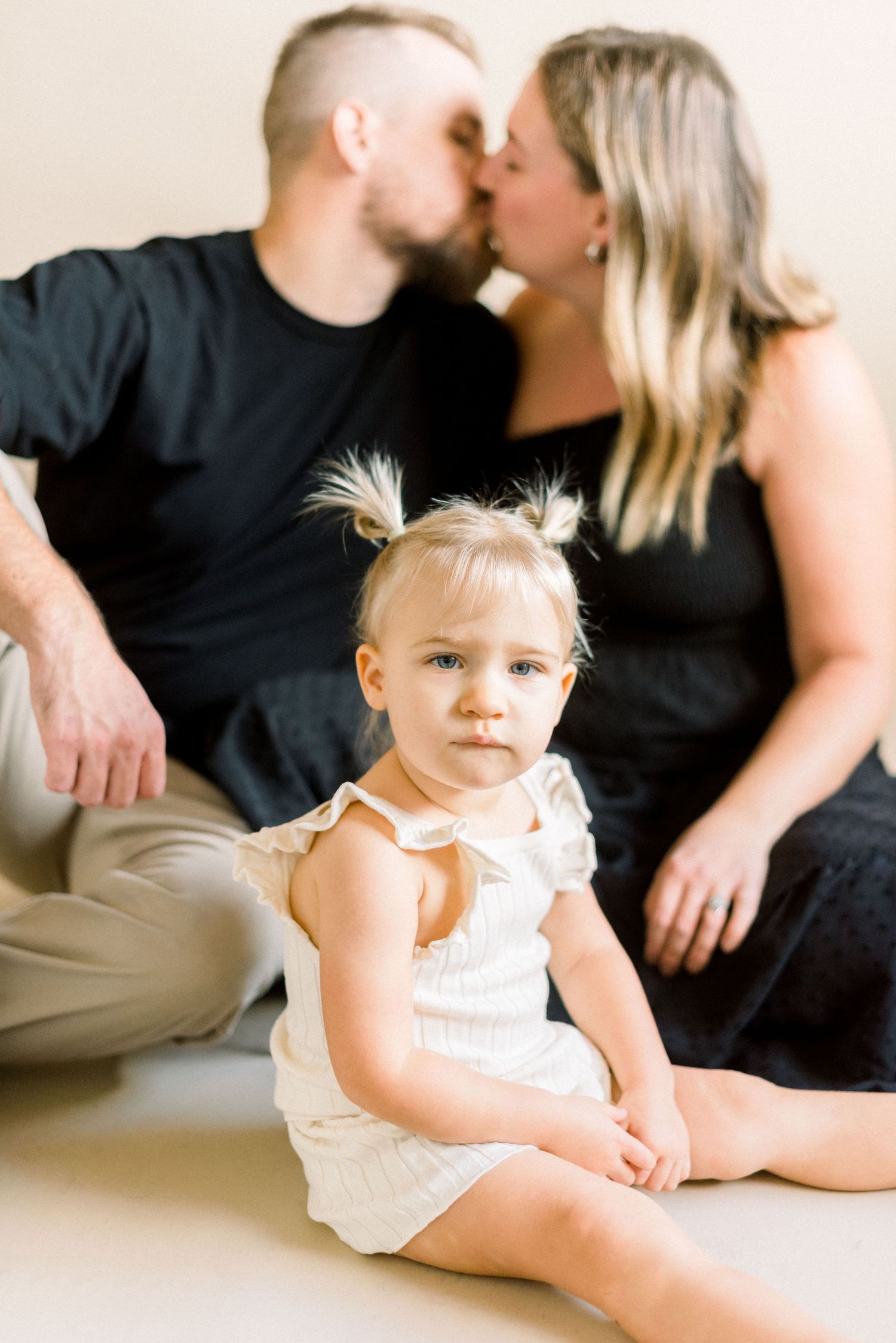 Intimate family portrait with parents sharing kiss while child sits in foreground.