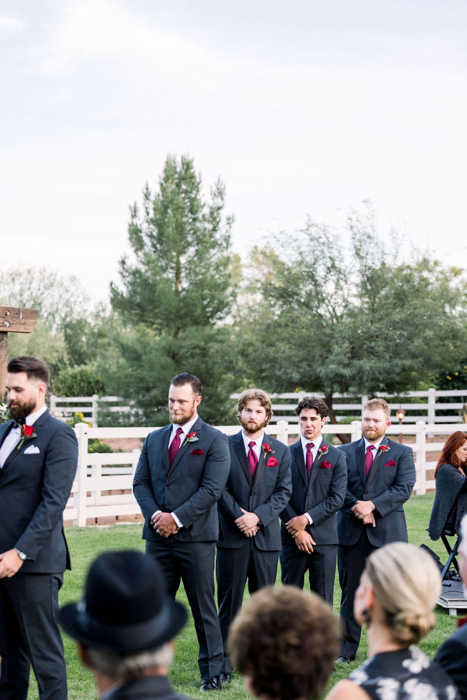 Groomsmen in navy suits stand in formation during an outdoor wedding ceremony.