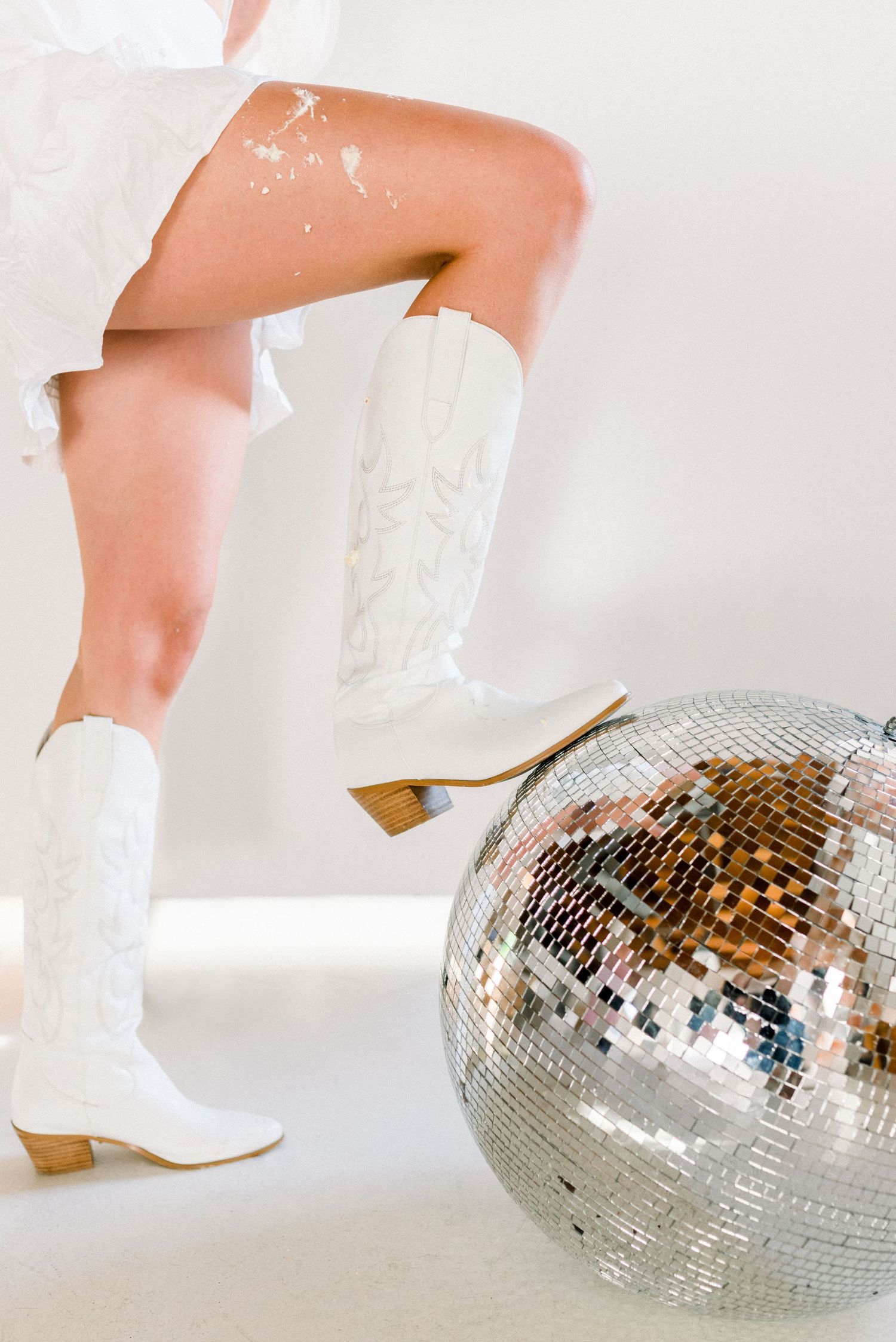 White western boots and a disco ball create a retro dance party vibe against a light background.