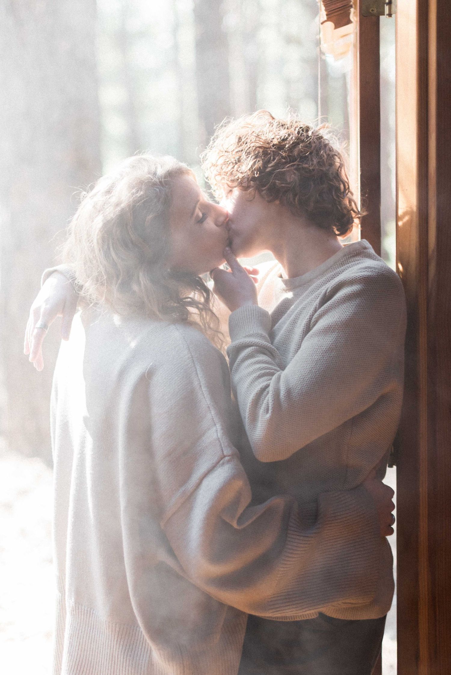 Romantic couple in matching sweaters sharing tender moment by window.