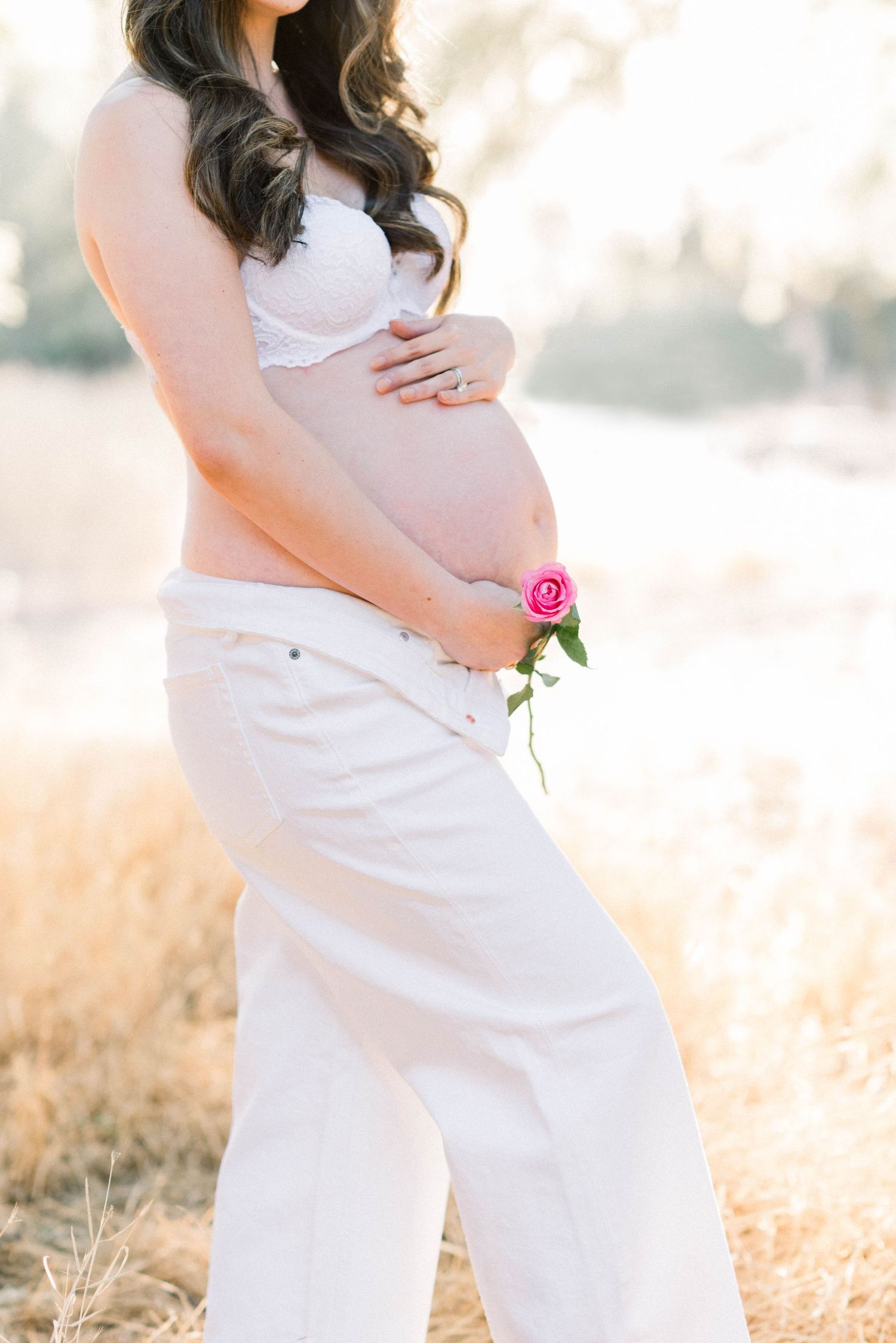 Side view maternity photo with single pink rose against sunlit background.
