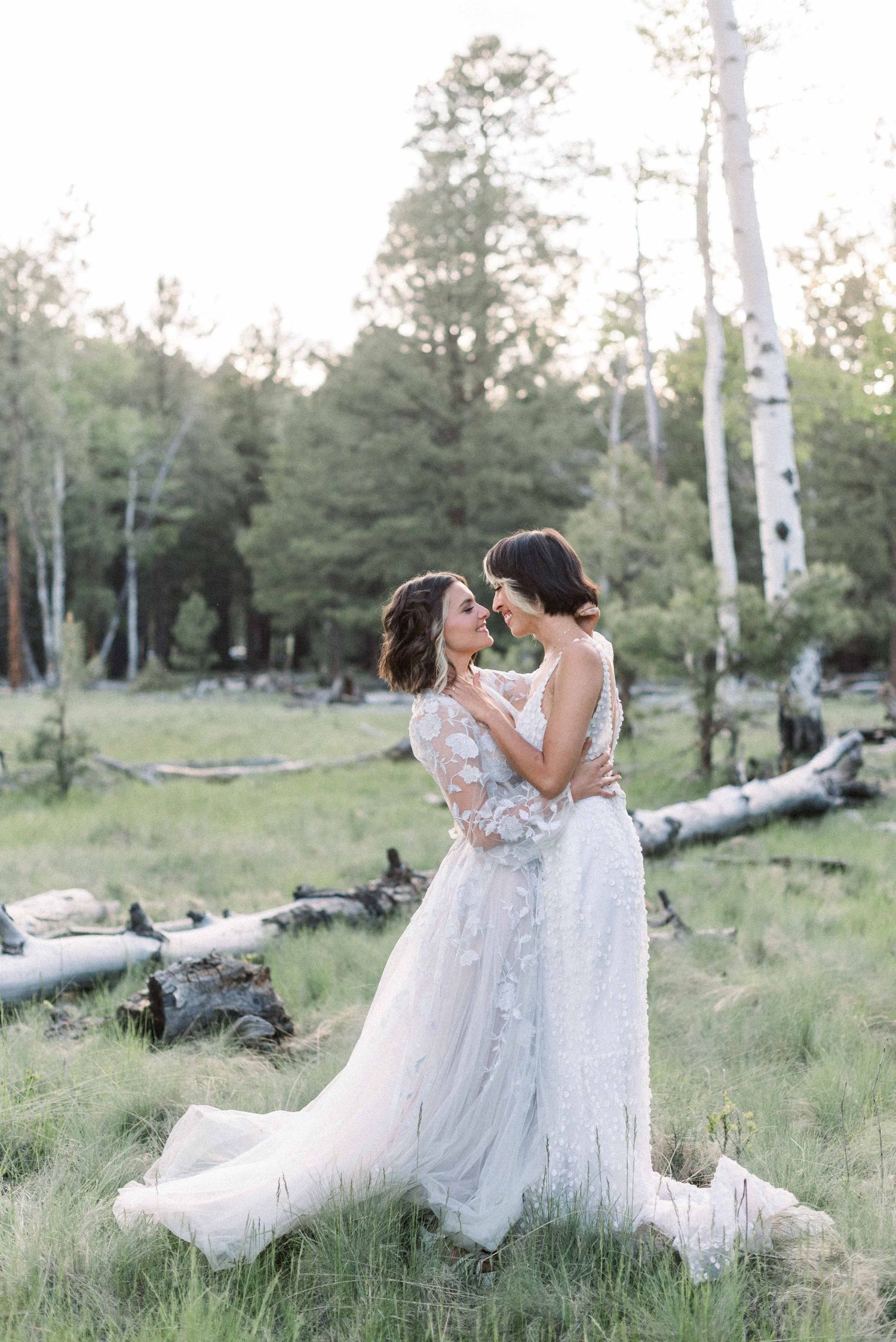 Romantic embrace between wedding couple in white dresses among aspen trees.