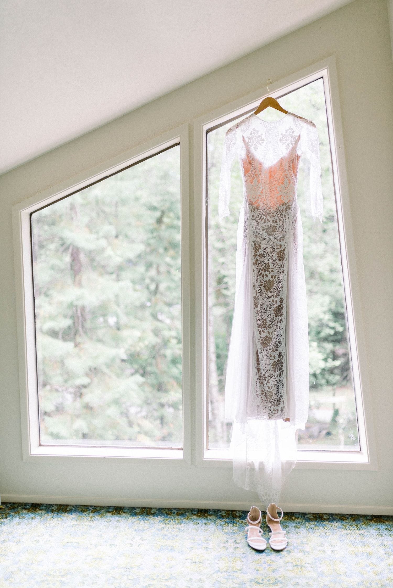 Delicate white lace wedding dress hanging in window with shoes below.