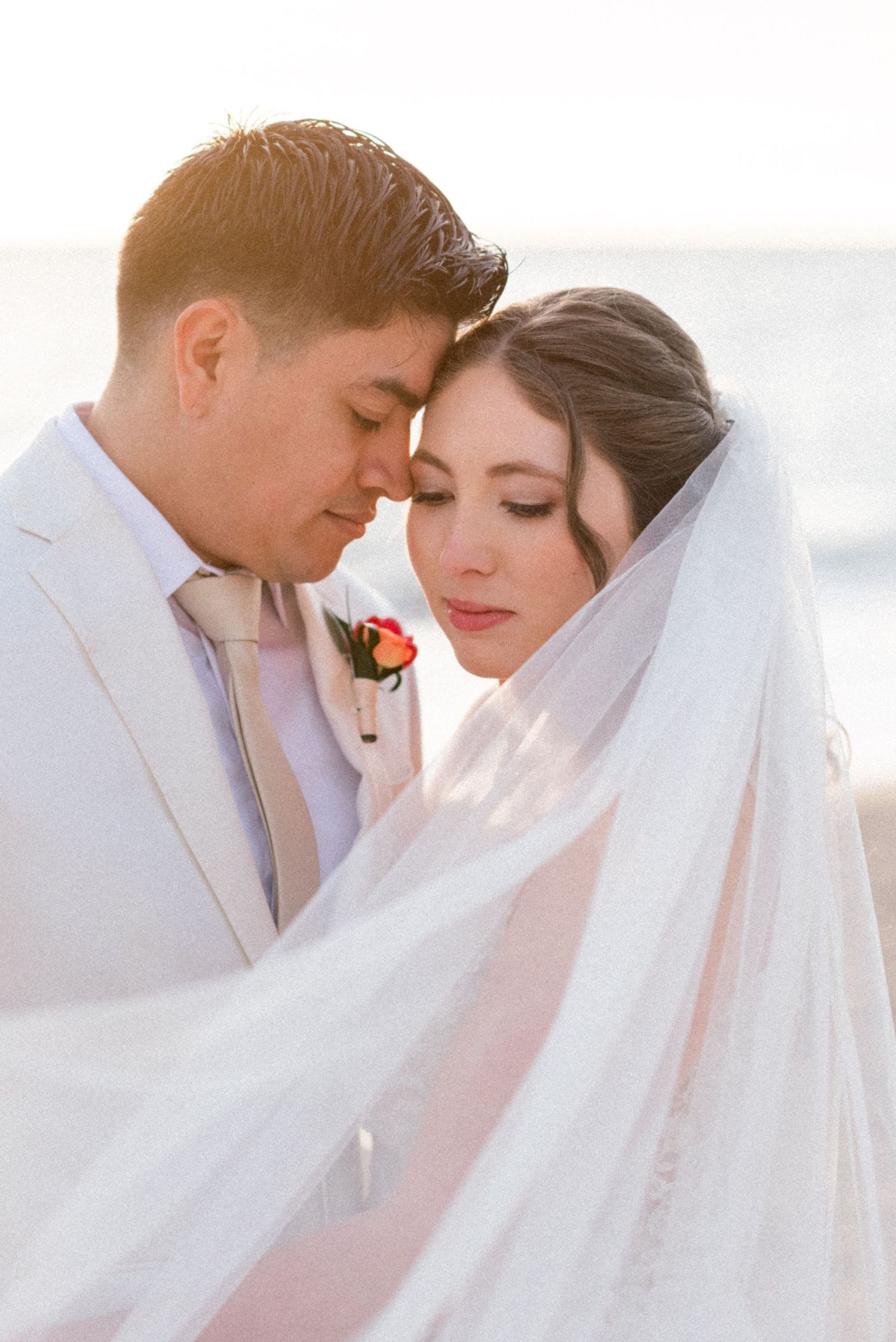 Intimate moment between newlyweds in soft beach lighting.