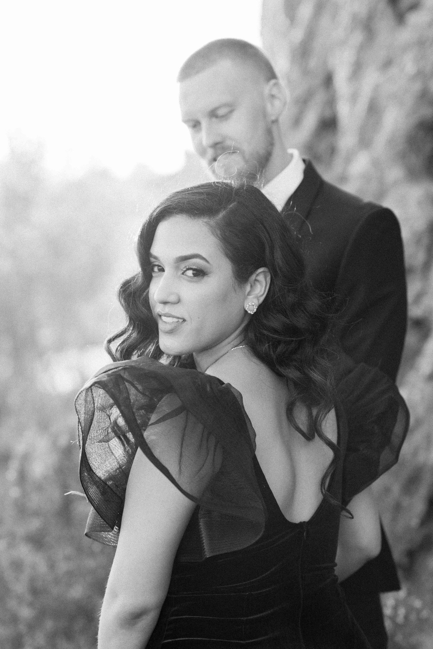 Black and white portrait of couple in formal attire against rocky backdrop.
