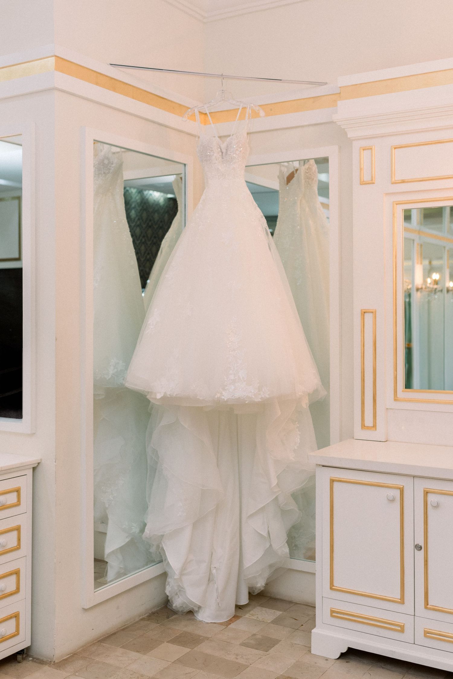White wedding dress hanging in elegant dressing room with gold trim details.