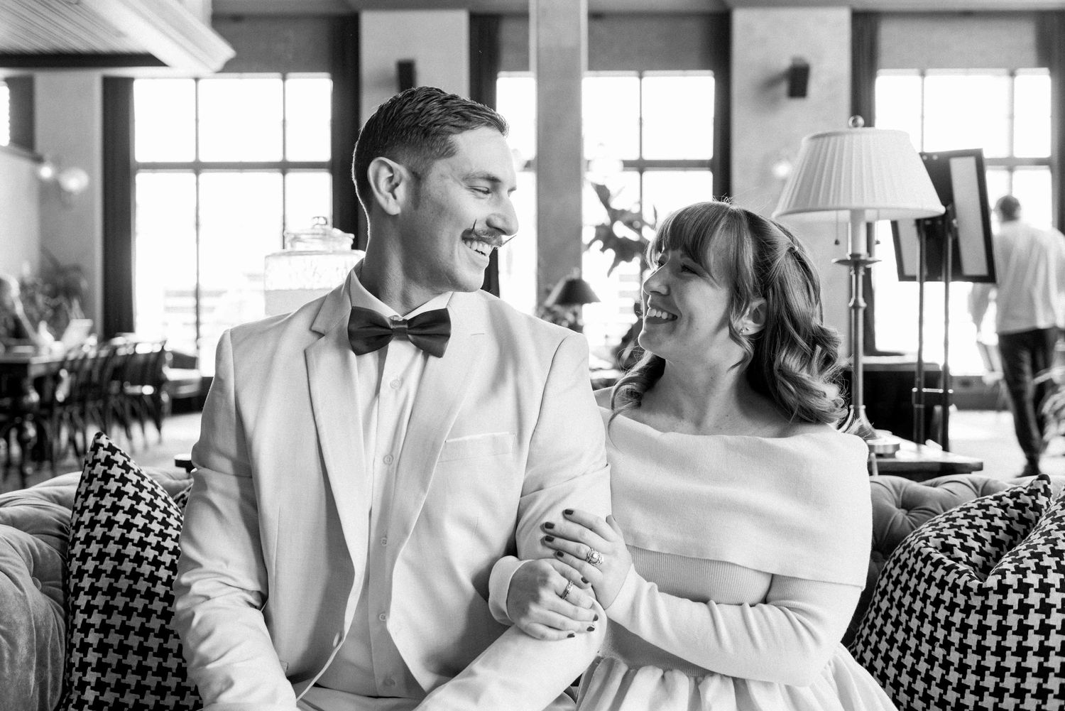 A couple sitting on a patterned couch shares a joyful moment in formal attire.