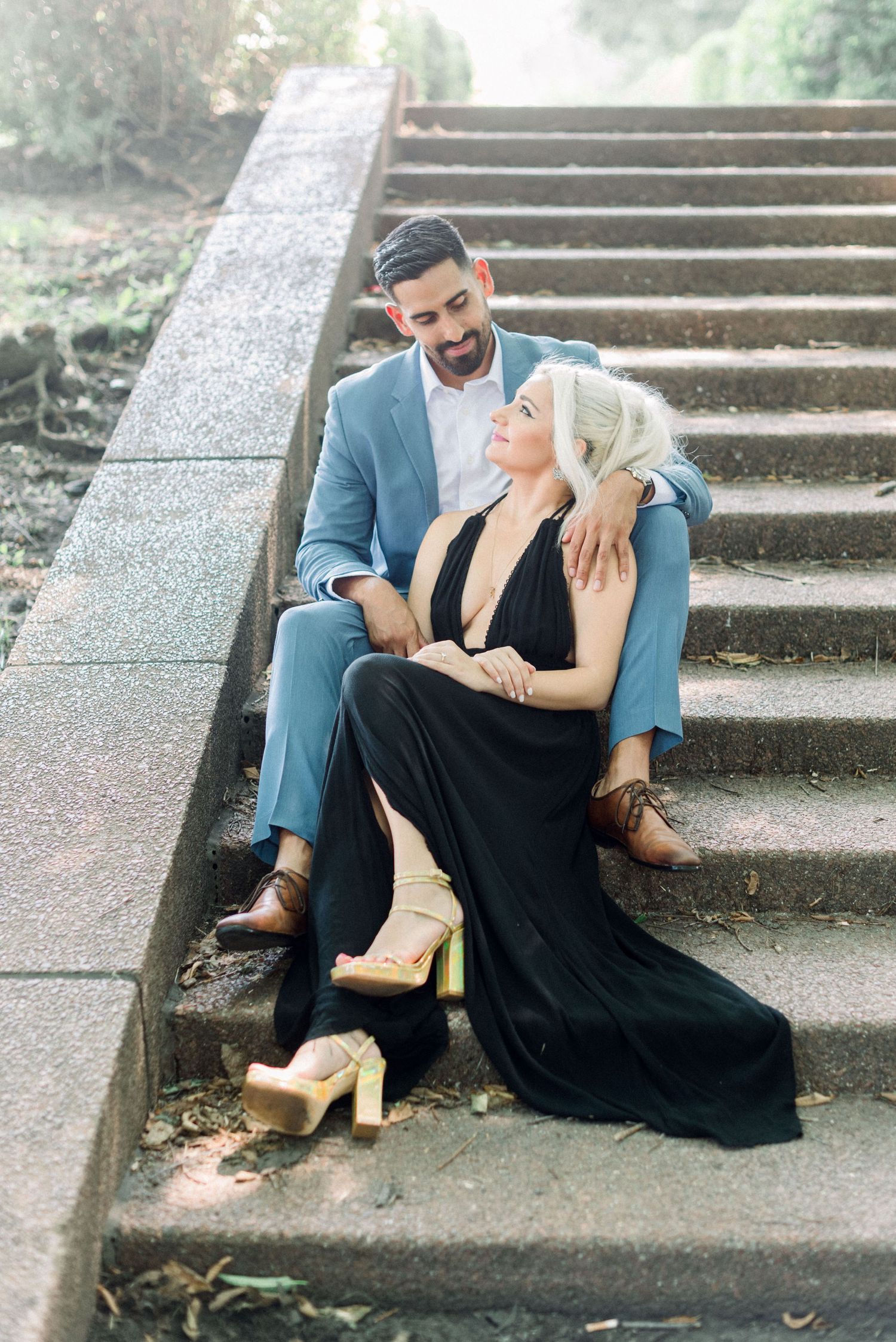 Couple dressed in formal attire sharing an intimate moment on stone steps in an outdoor garden setting.