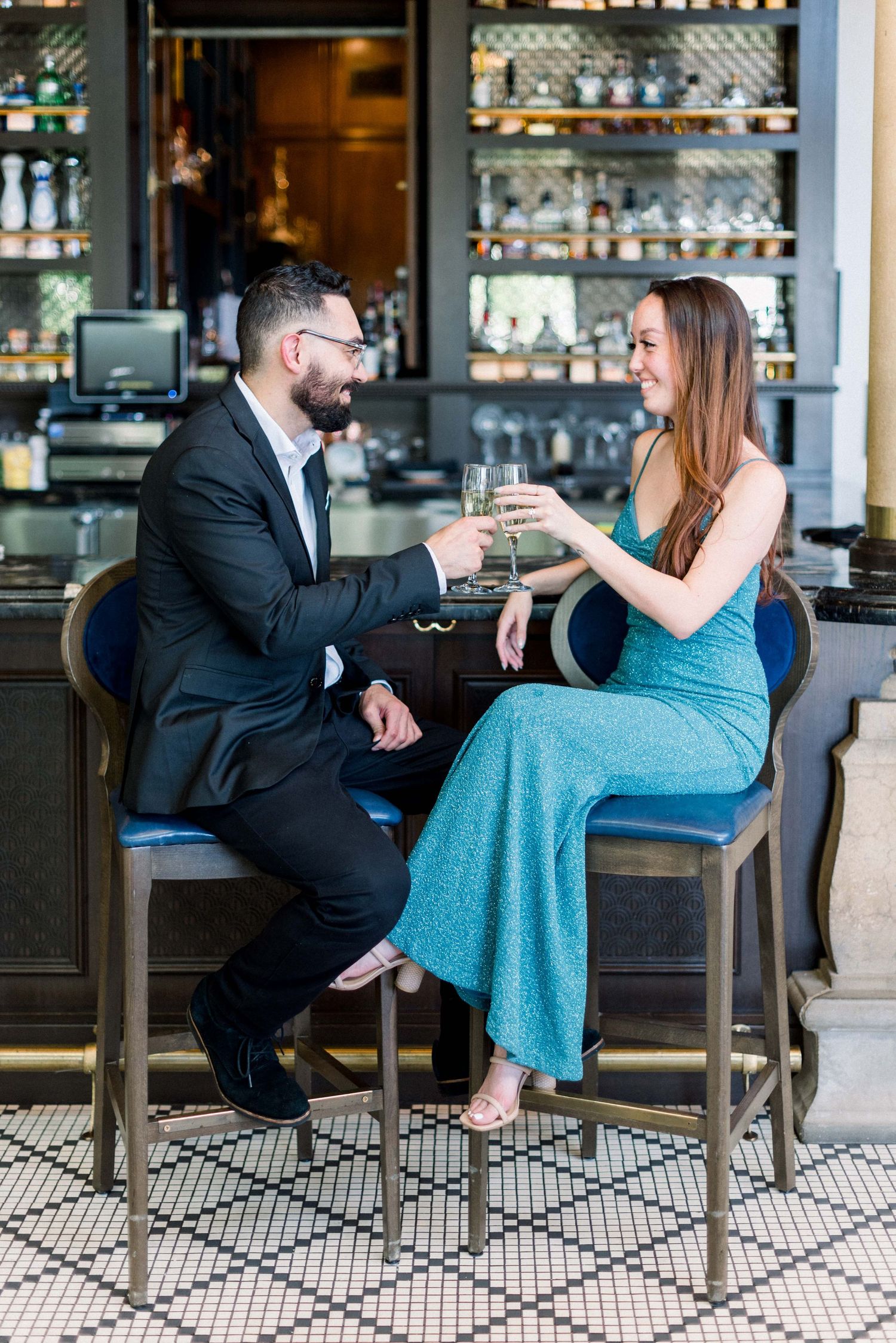A couple toasts with champagne at an upscale bar featuring elegant glassware displays.