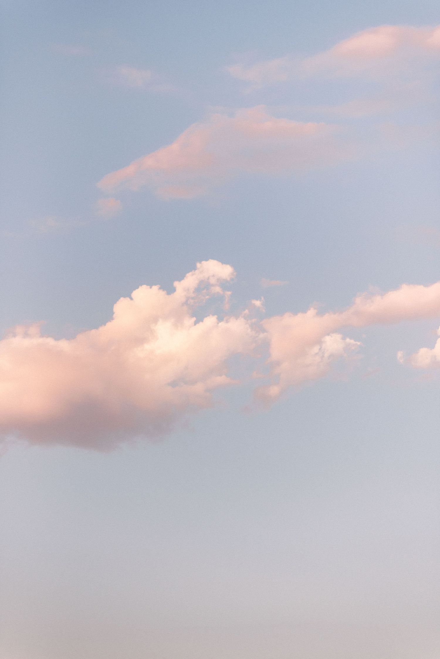 Soft pink clouds floating in a pastel blue sky during sunset.