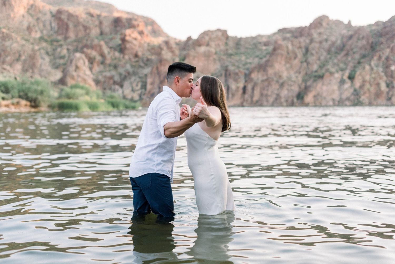 Couple stands in lake water with dramatic rocky cliffs behind them during their engagement shoot.