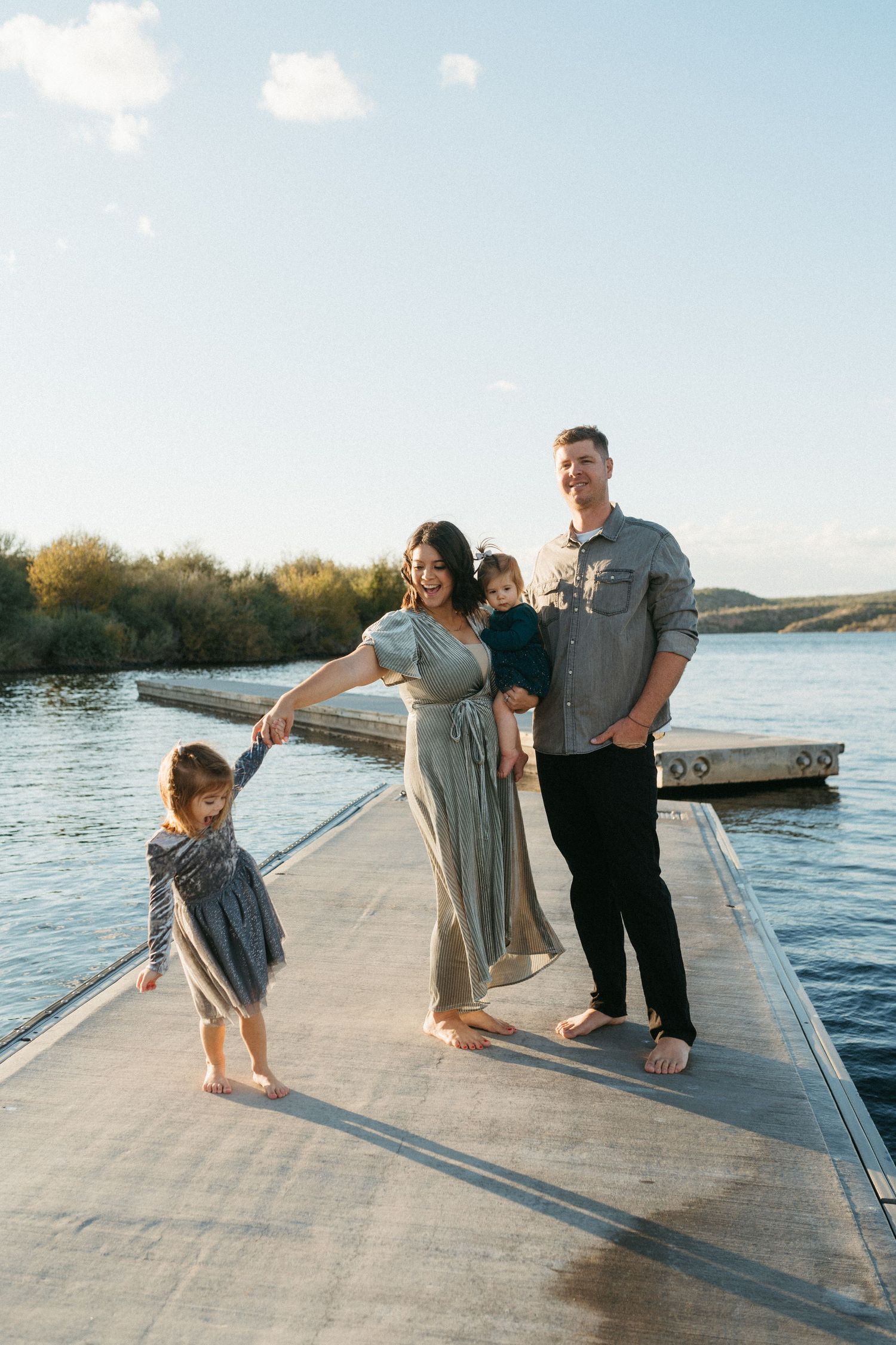 Family enjoying a sunset moment together on a wooden dock by a peaceful lake.