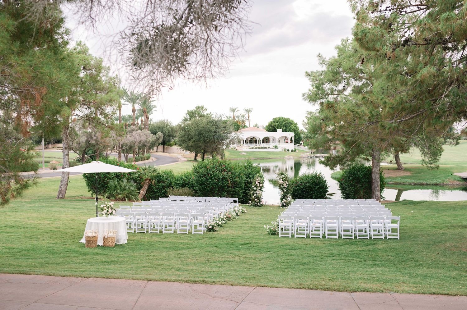 White chairs arranged on a lush green lawn for an outdoor wedding ceremony.