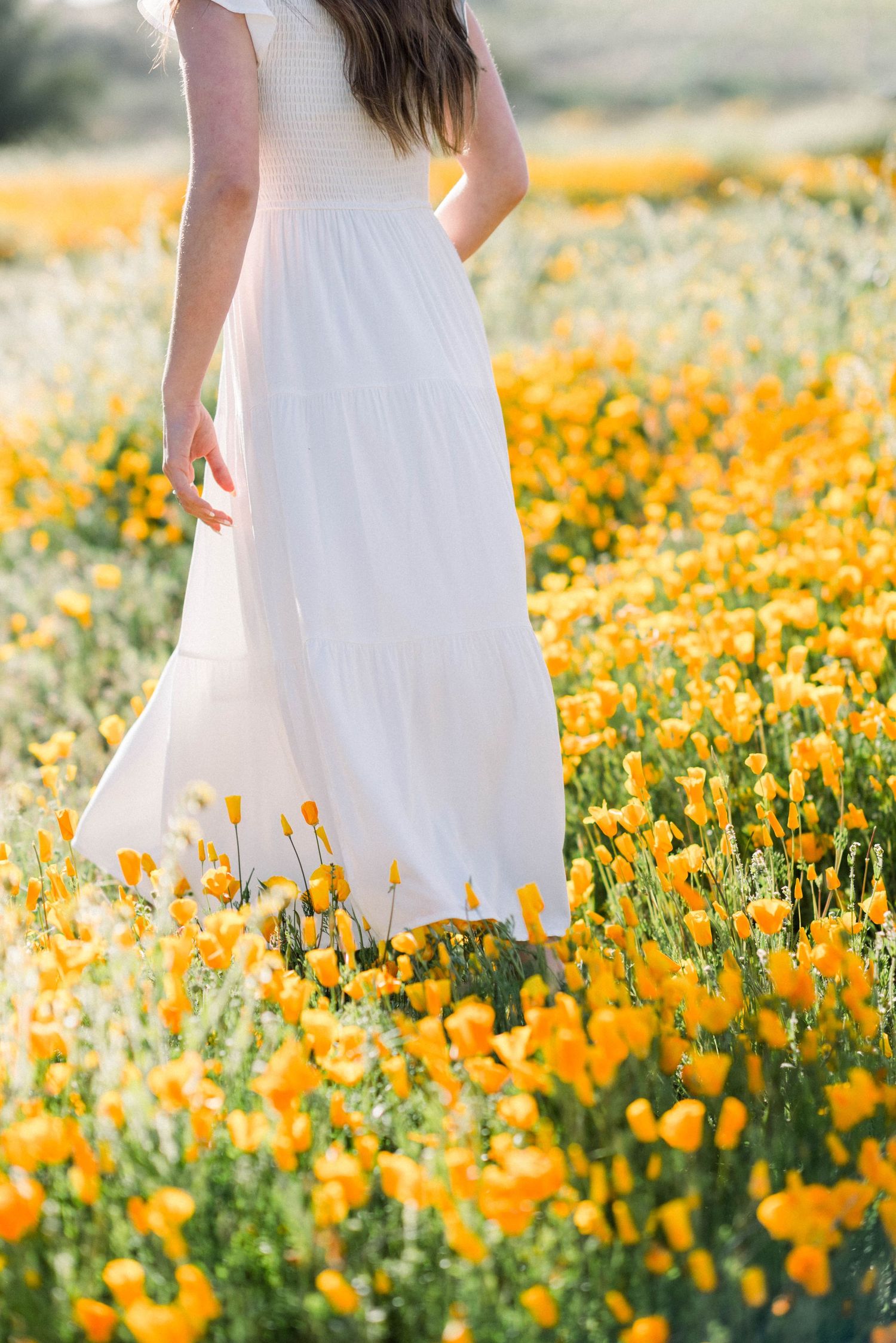 A flowing white dress billows among a vibrant field of golden California poppies.