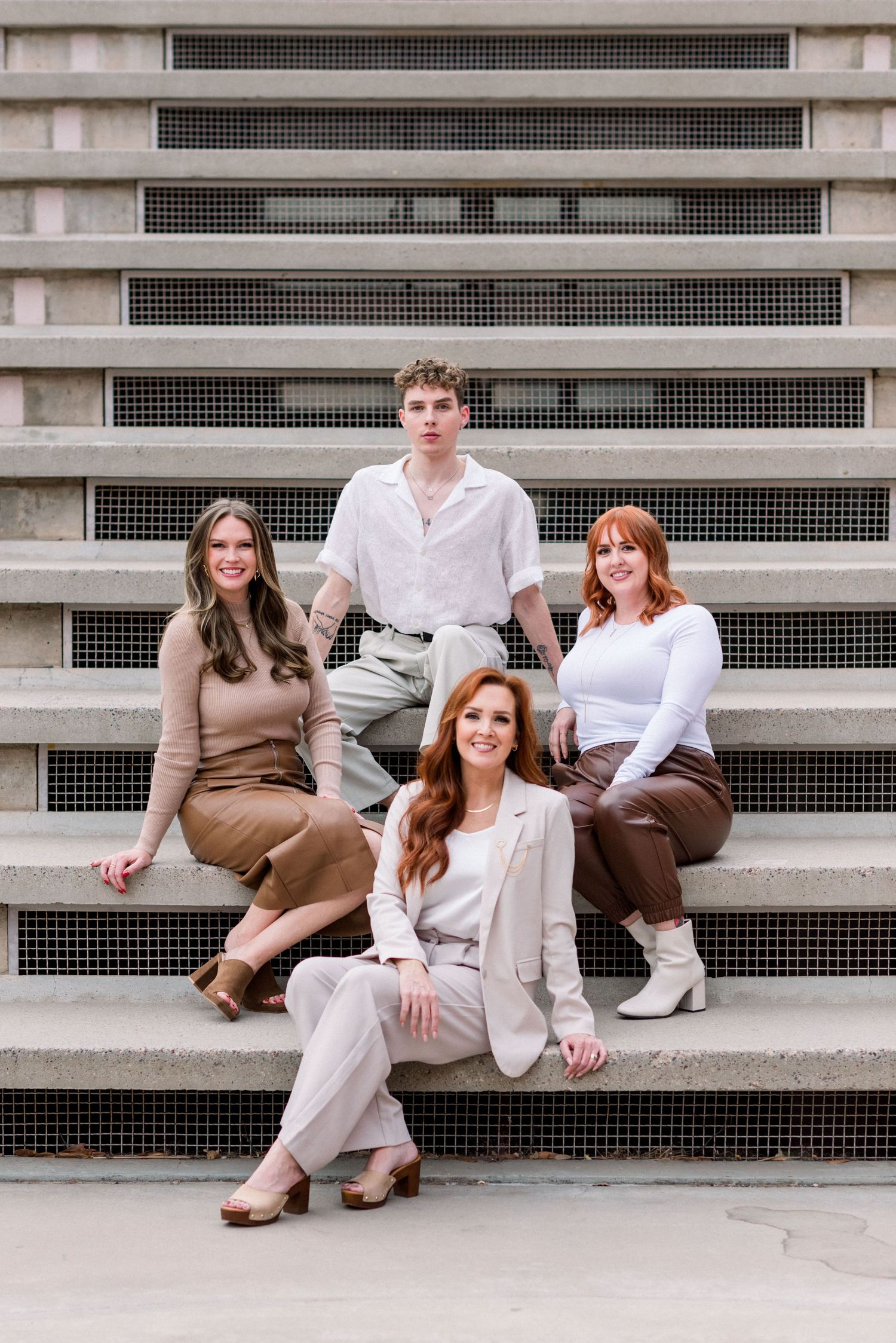 Four people in coordinated neutral-toned outfits pose casually on concrete stadium-style steps.