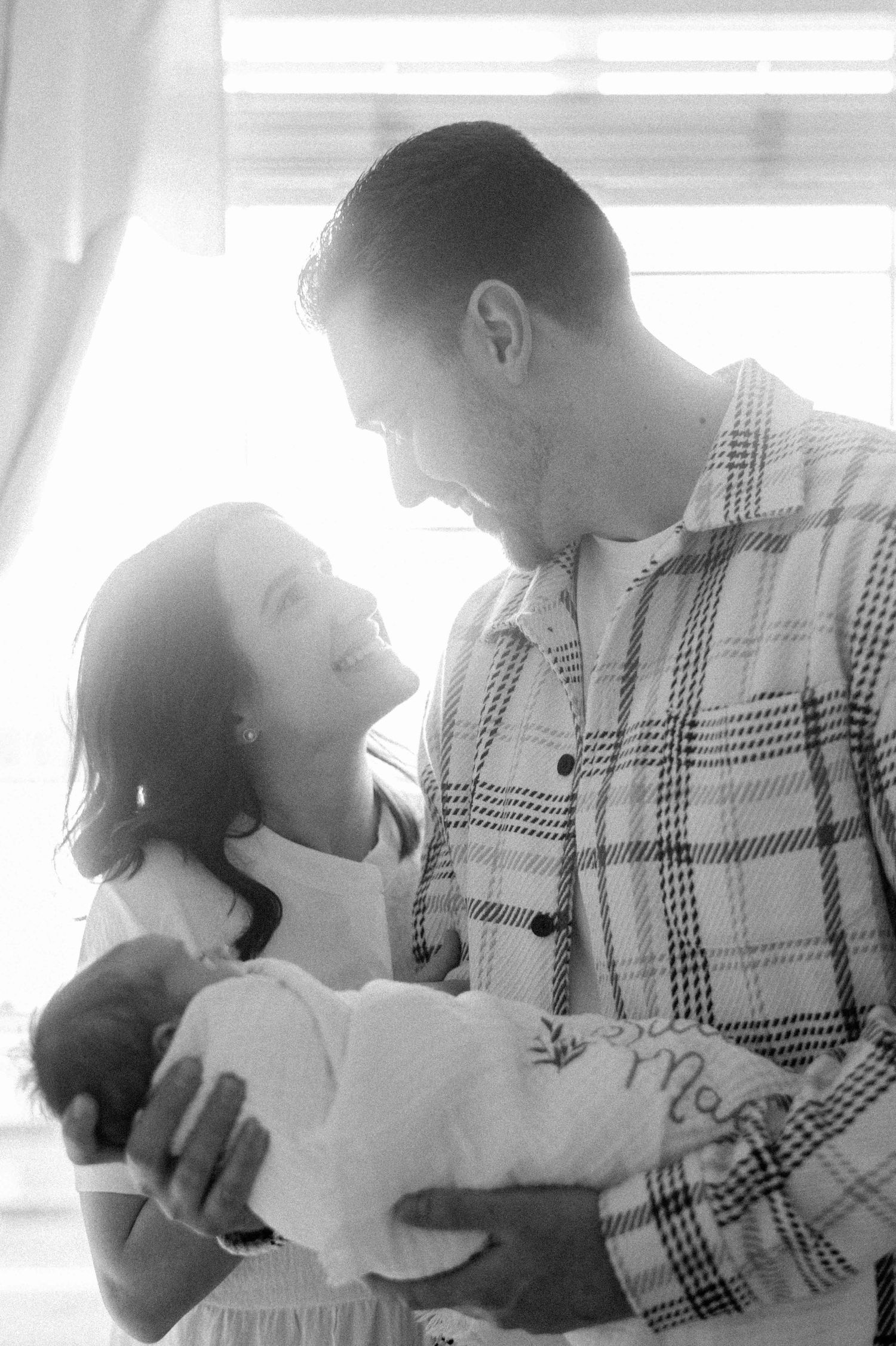 A black and white capture of a couple sharing loving glances while holding their baby.