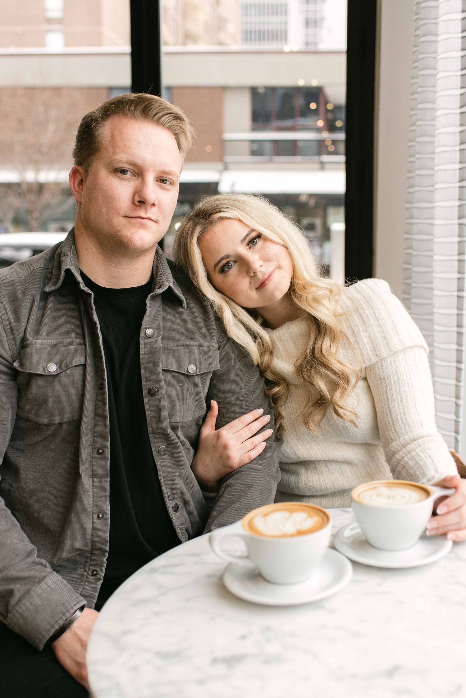 Couple enjoying coffee at a modern cafe with marble tables and city views.