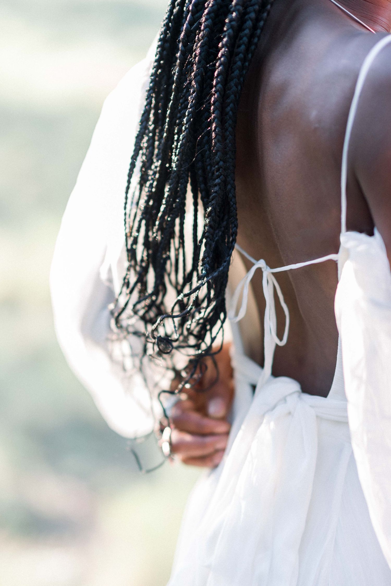 Close-up detail of long braided hair and white dress against soft natural lighting.
