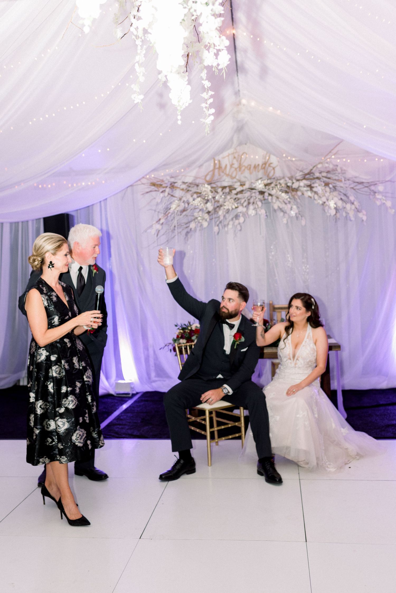 Wedding reception scene with guests toasting and celebrating in an elegantly decorated white tent venue.