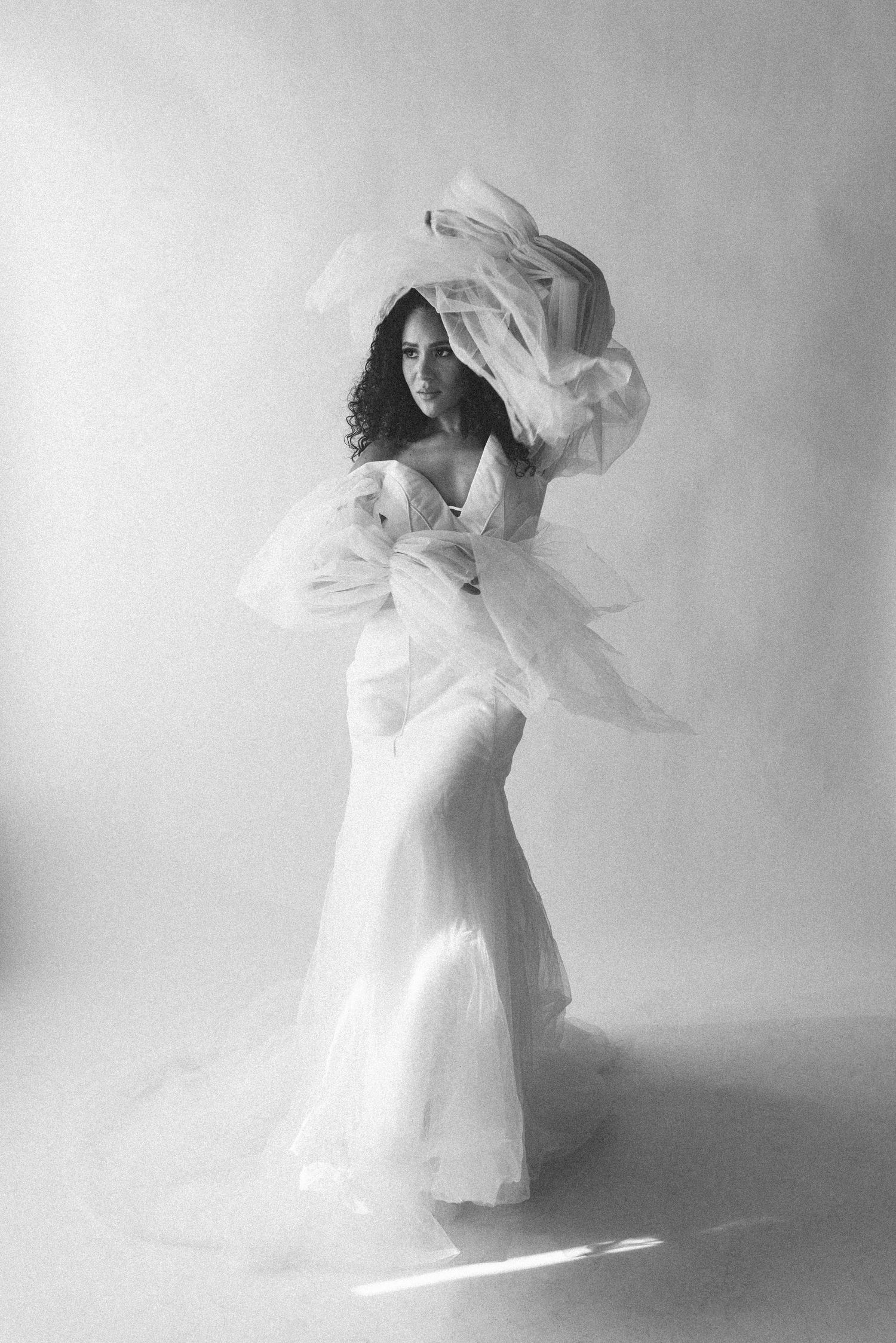 Black and white photo of bride in elegant dress with floating fabric elements.