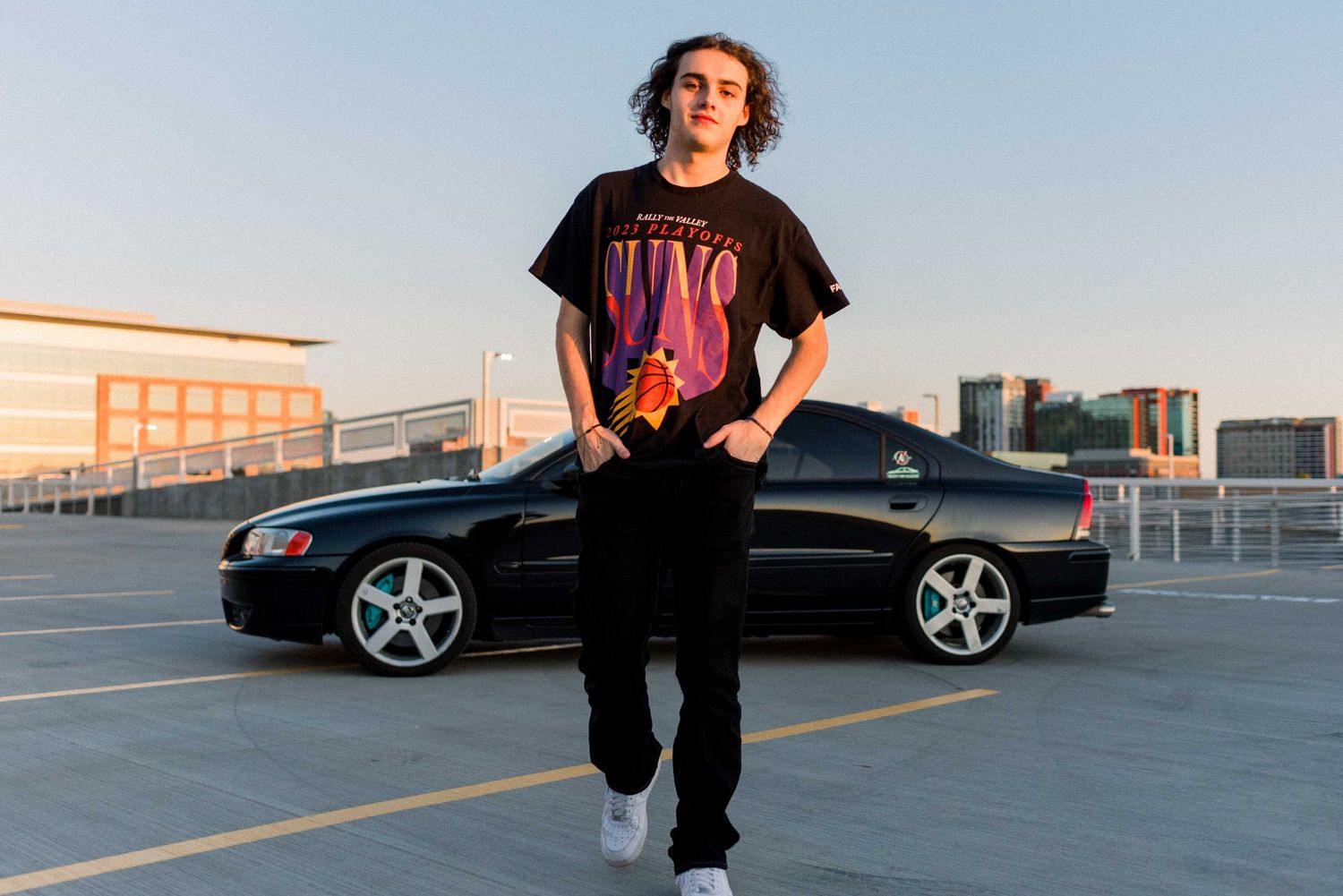 Person in graphic t-shirt standing next to black sedan on rooftop.