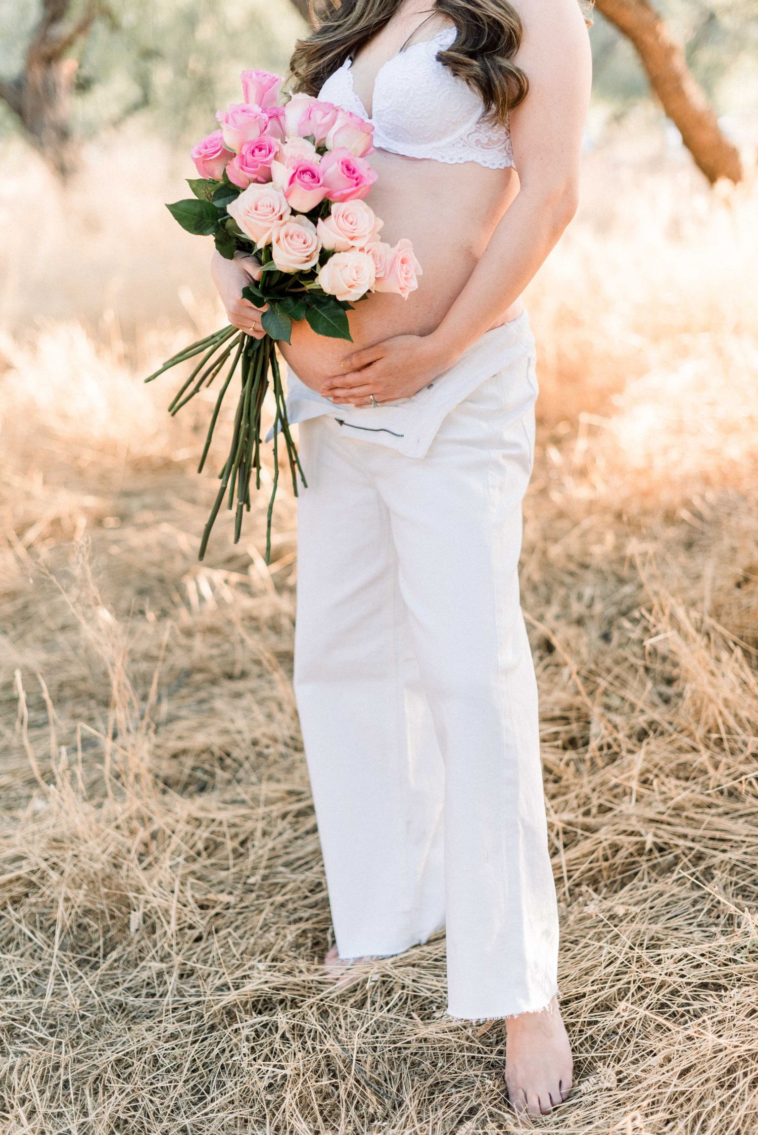 Pink rose bouquet held against white clothing in golden field.