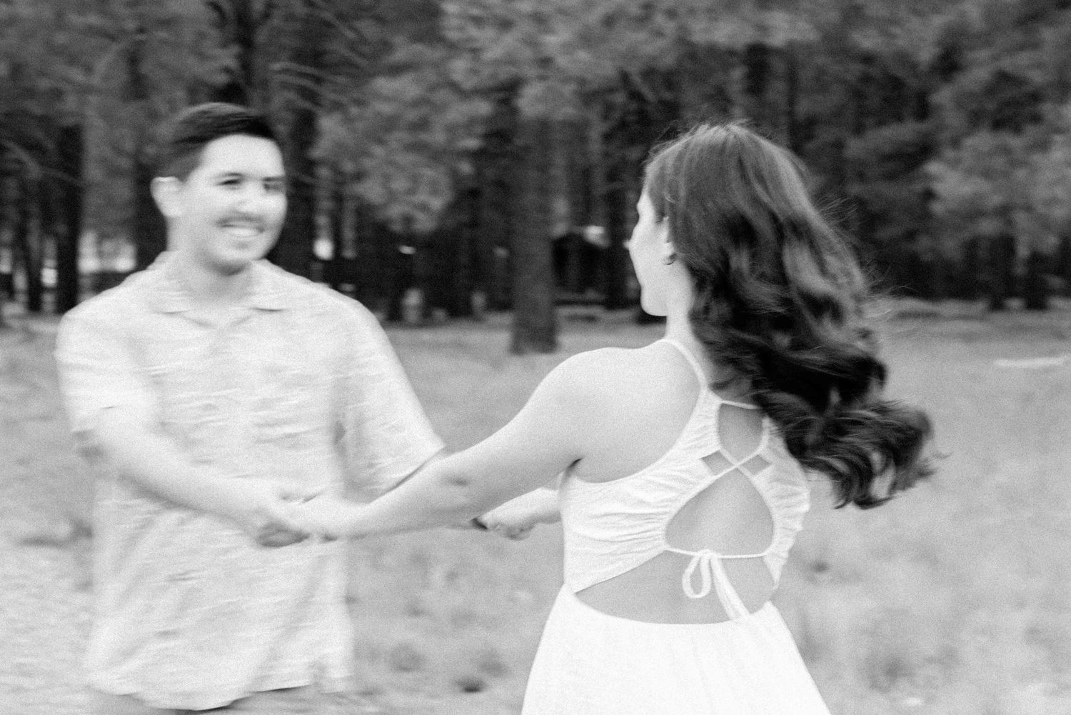 A couple shares a playful moment dancing together in a sun-drenched outdoor setting.