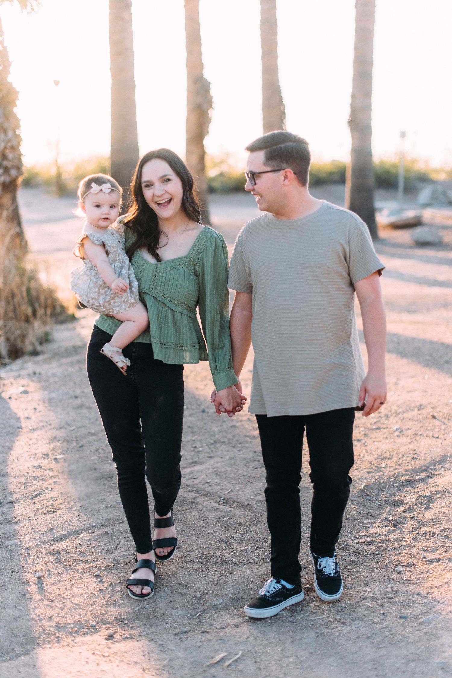 Family walking hand in hand on a palm tree lined path during sunset.